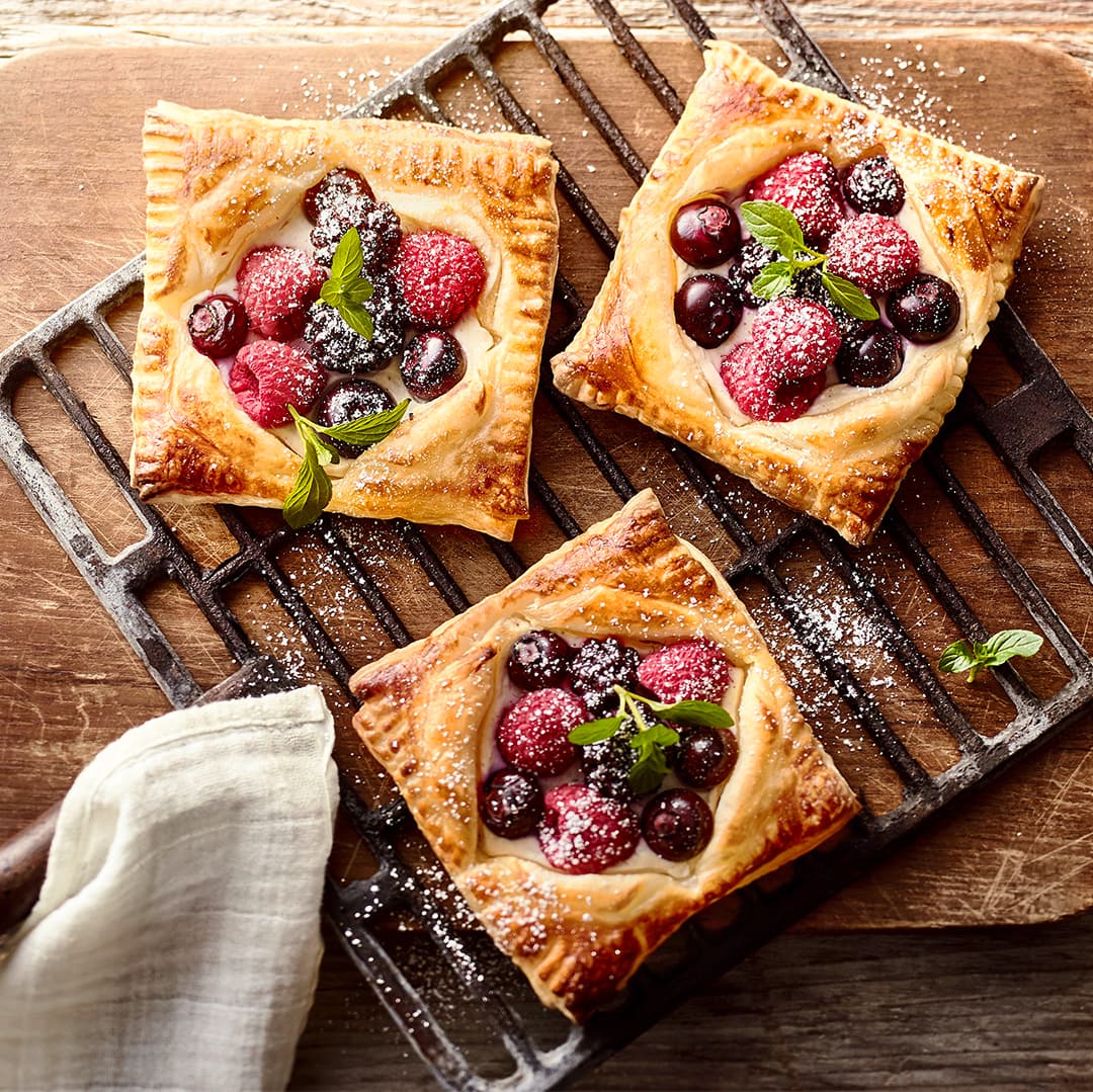 Vierecken aus goldgelb gebackenem Blätterteig mit Himbeeren, Blaubeeren und Brombeeren, auf einem Grillrost