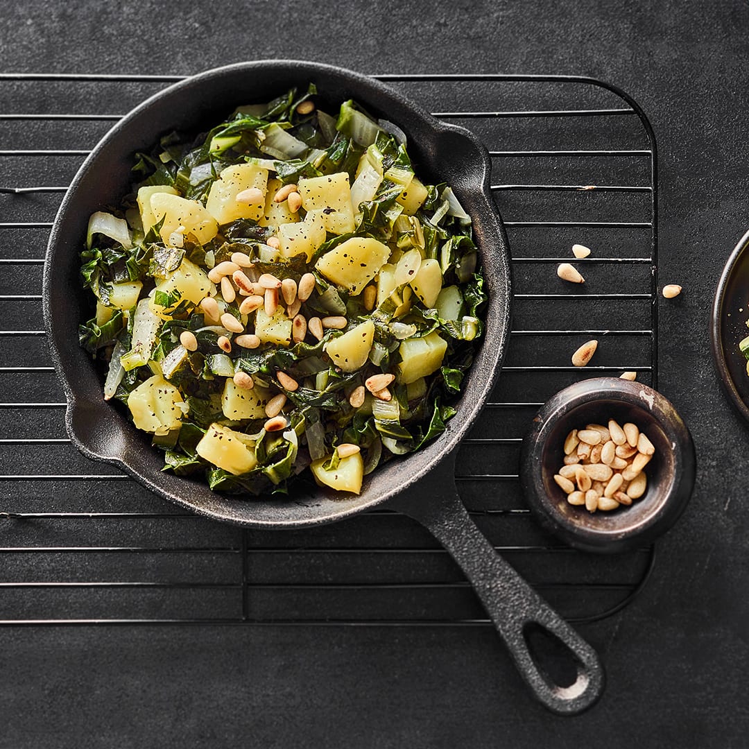 Mangold und Kartoffeln mit Knoblauch und Zwiebeln in einer gusseisernen Pfanne auf einem Abkühlgitter