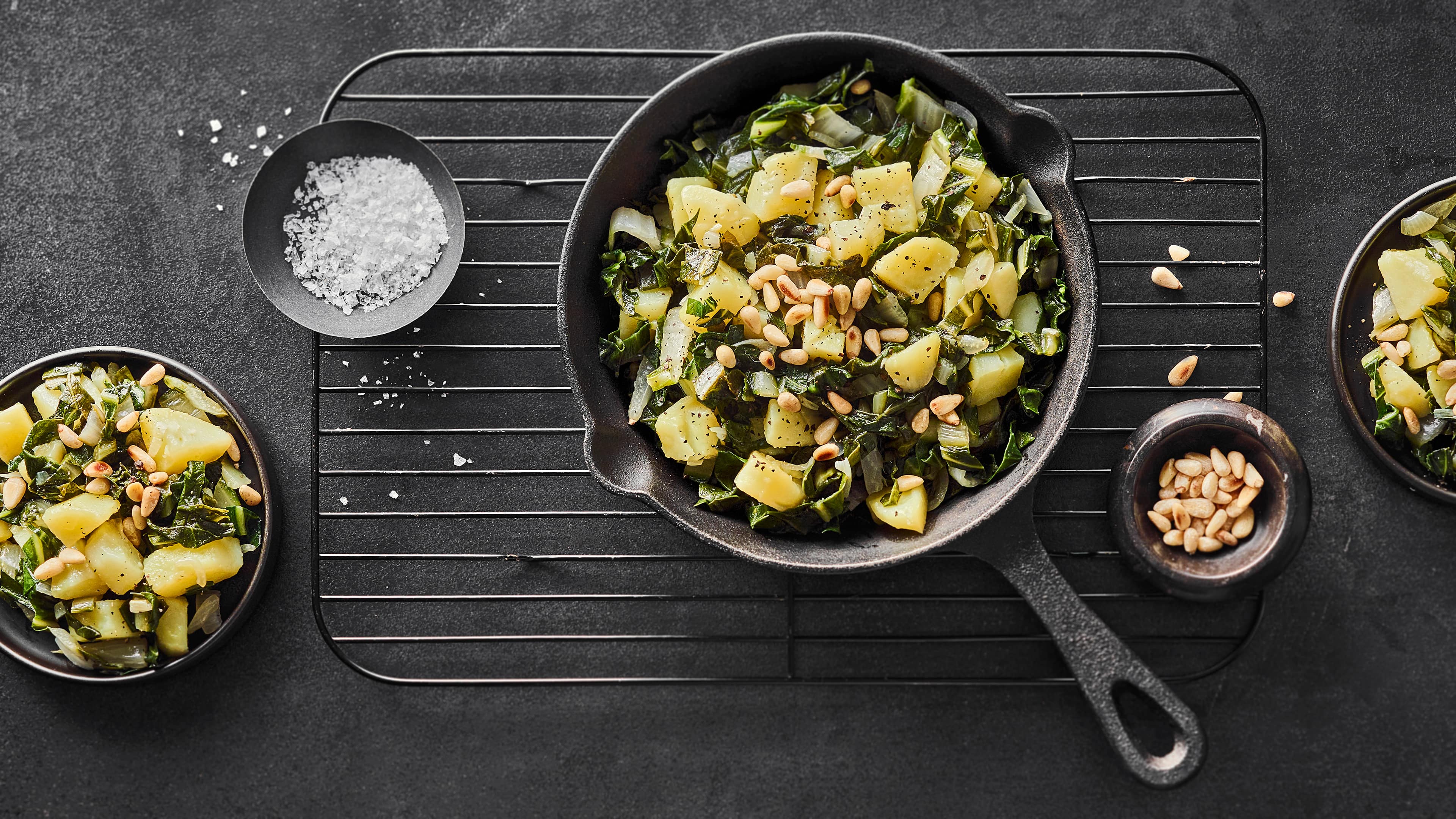 Kroatisches Rezept für Blitva aus Mangold und Kartoffeln Mangold und Kartoffeln mit Knoblauch und Zwiebeln in einer gusseisernen Pfanne auf einem Abkühlgitter