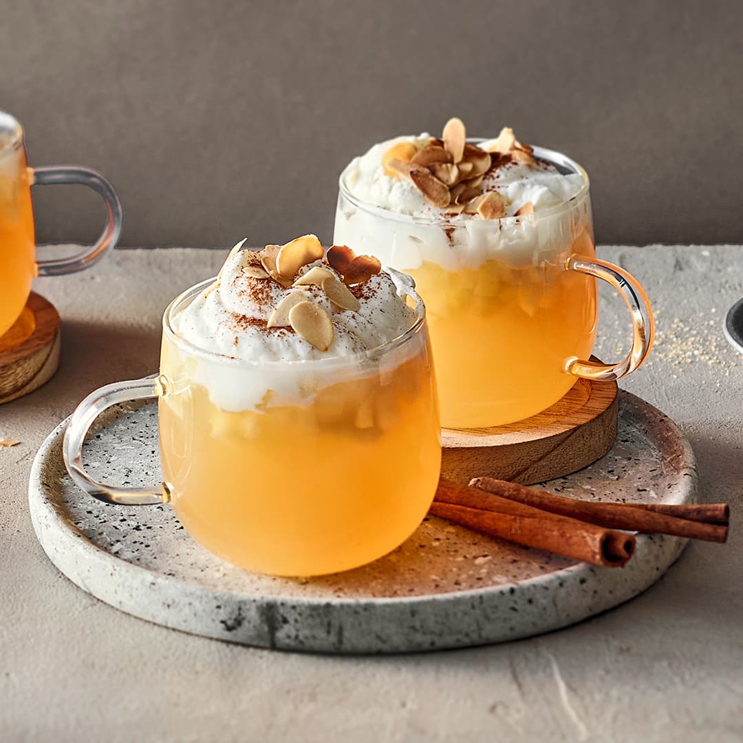 Bauchige Glastassen gefüllt mit Punsch mit kleinen Apfelstückchen, getoppt mit Schlagsahne, Zimt und Mandelblättchen