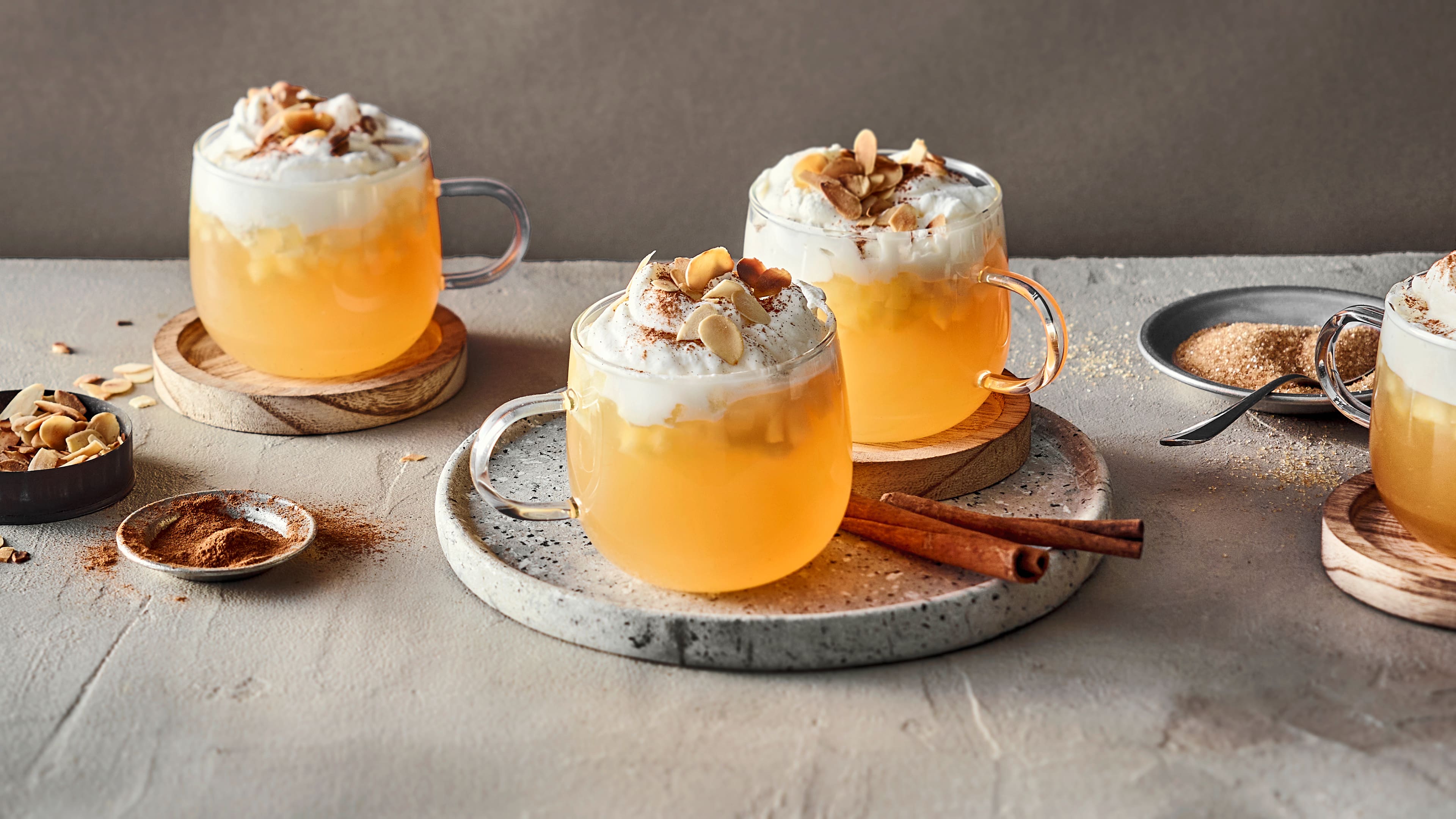 Bauchige Glastassen gefüllt mit Punsch mit kleinen Apfelstückchen, getoppt mit Schlagsahne, Zimt und Mandelblättchen
