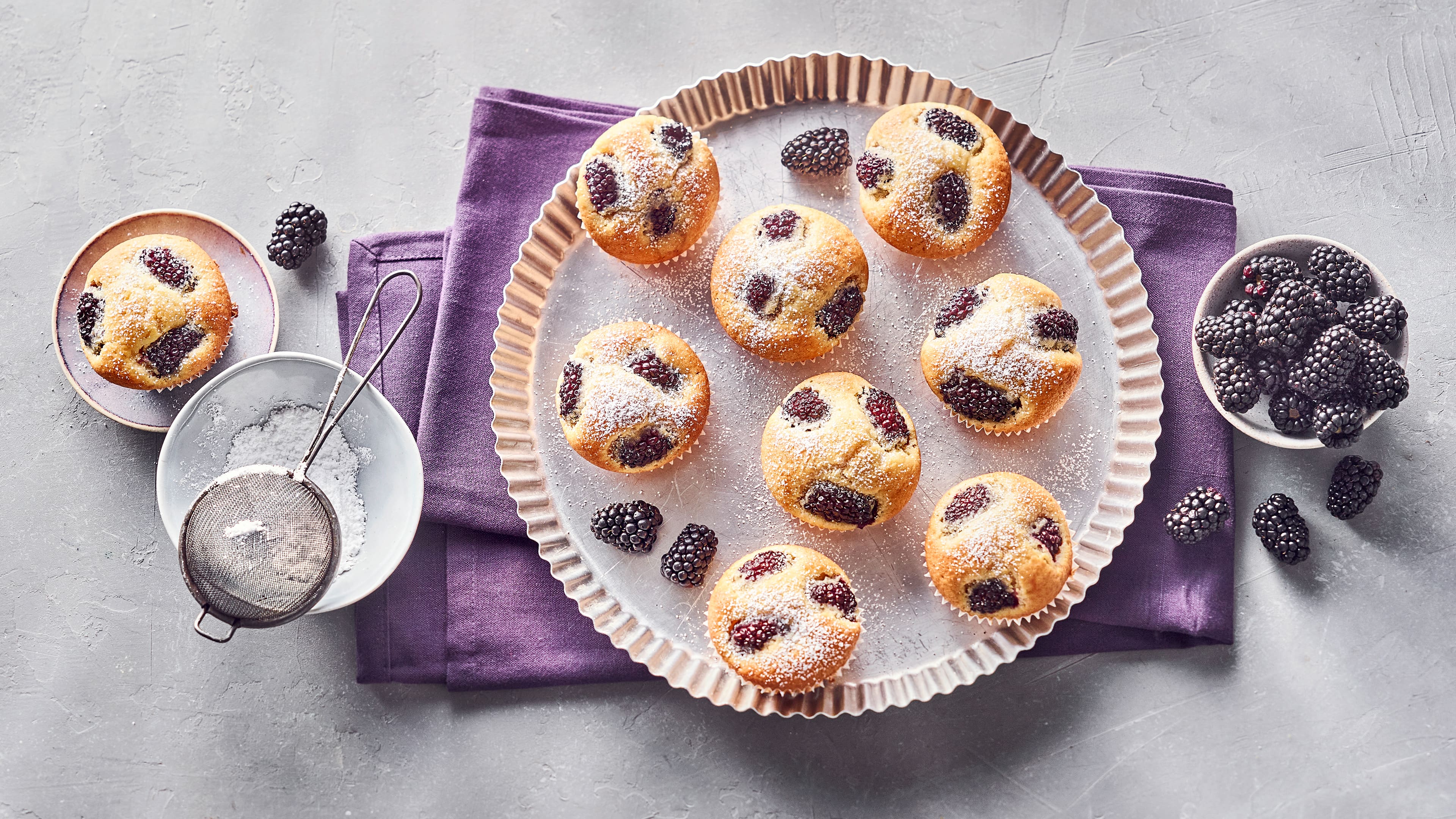 Rezept für Brombeer Muffins Helle Muffins mit dunklen Brombeeren auf einem runden Tablett