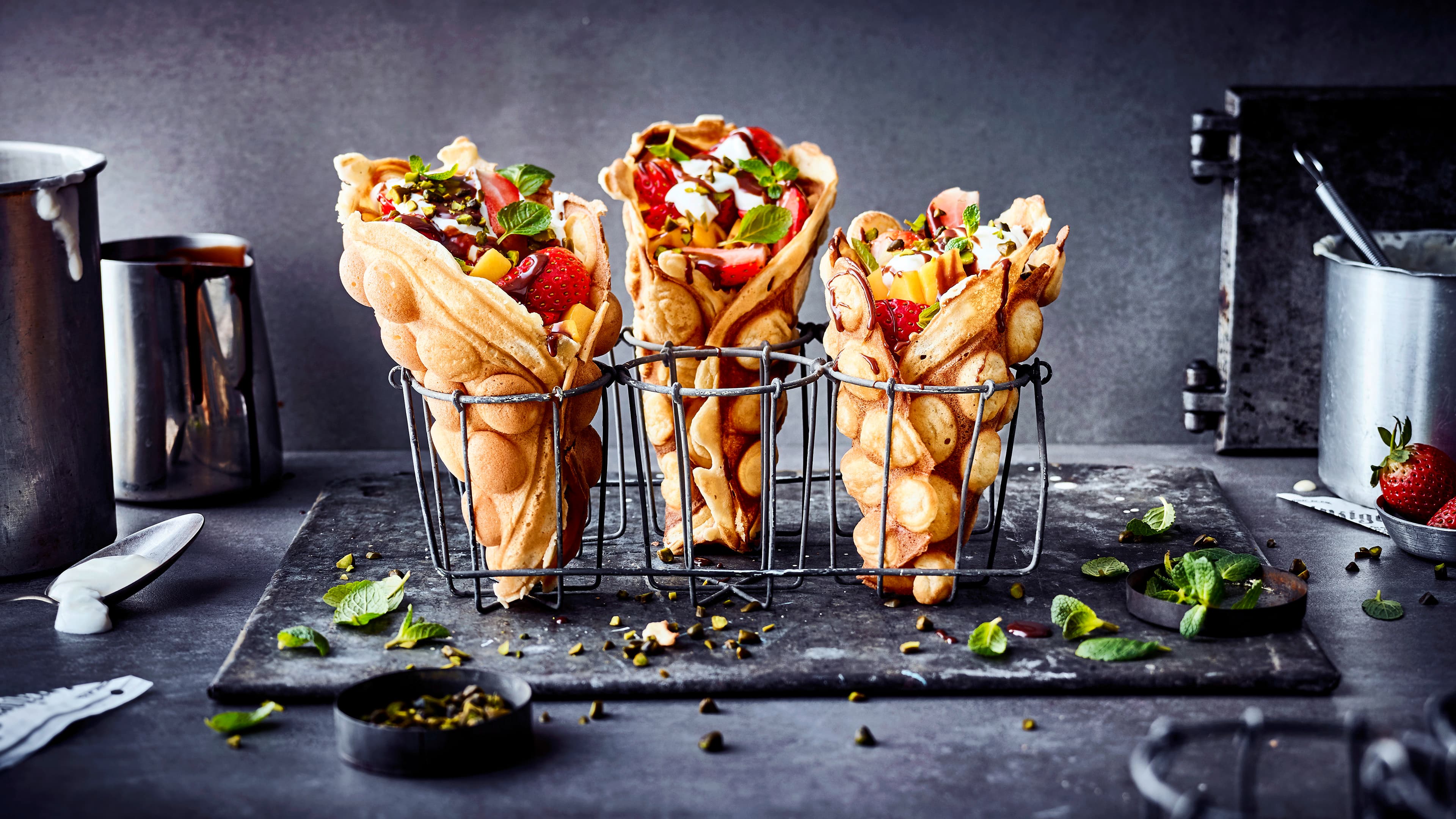 Hügelige Waffeln, gerollt in Trichterform, befüllt mit Mango, Erdbeeren und weißer Creme, aufgestellt in Drahtkörbchen