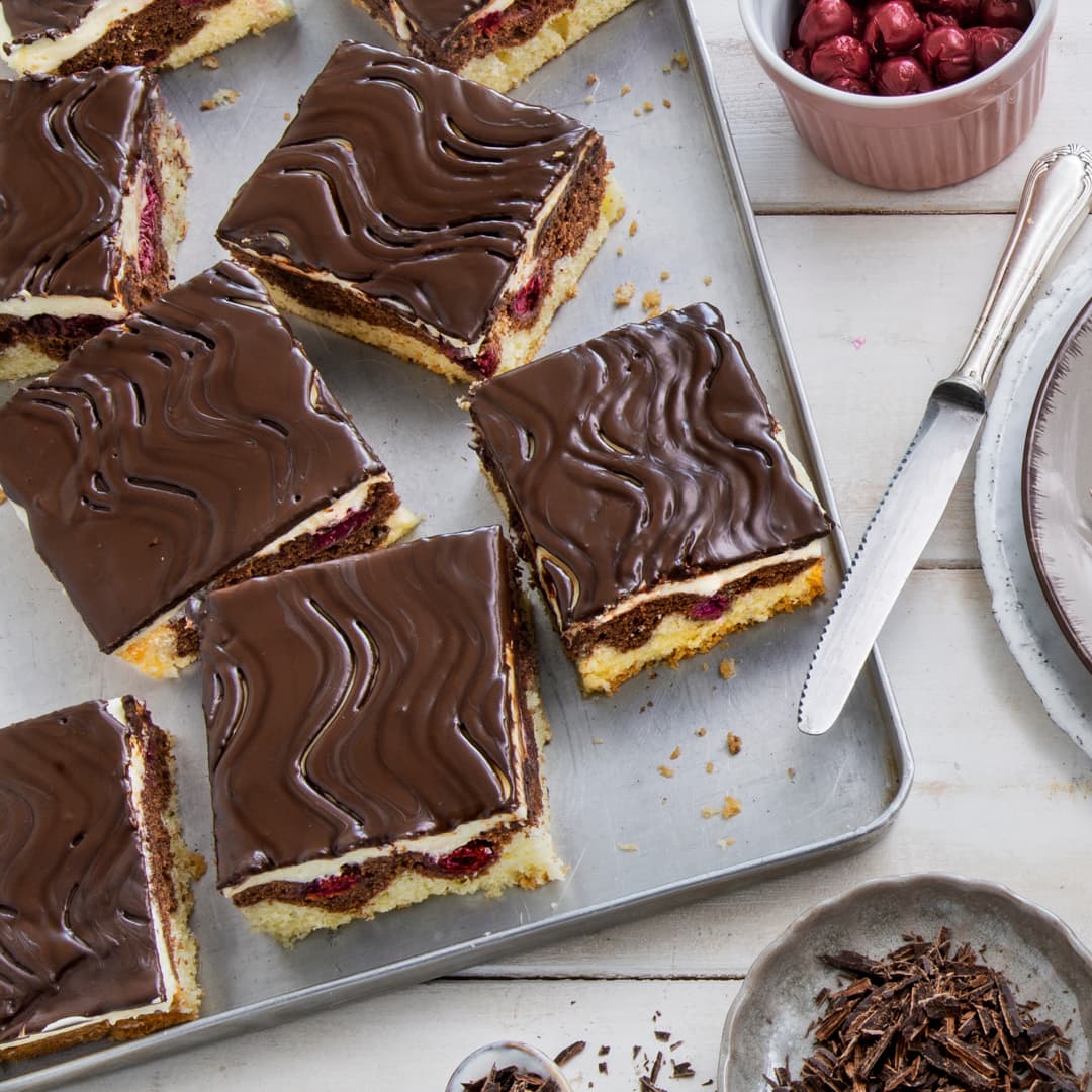 Typisches Wellenmuster auf der Schokolade, zweifarbiger Kuchenteig, fruchtige Kirschen und Buttercreme – das macht eine Donauwelle aus. Mit unserem Rezept gelingt Ihnen der Klassiker.