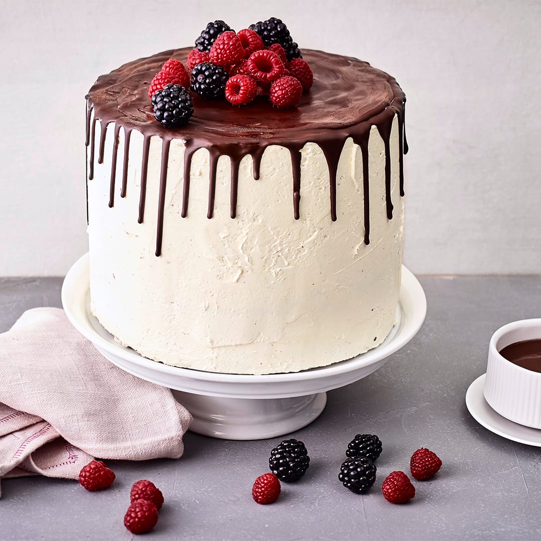 Eine weiße Creme-Torte mit Zartbitter-Glasur, die am Rand der Torte runtergelaufen ist, auf einer weißen Etagere