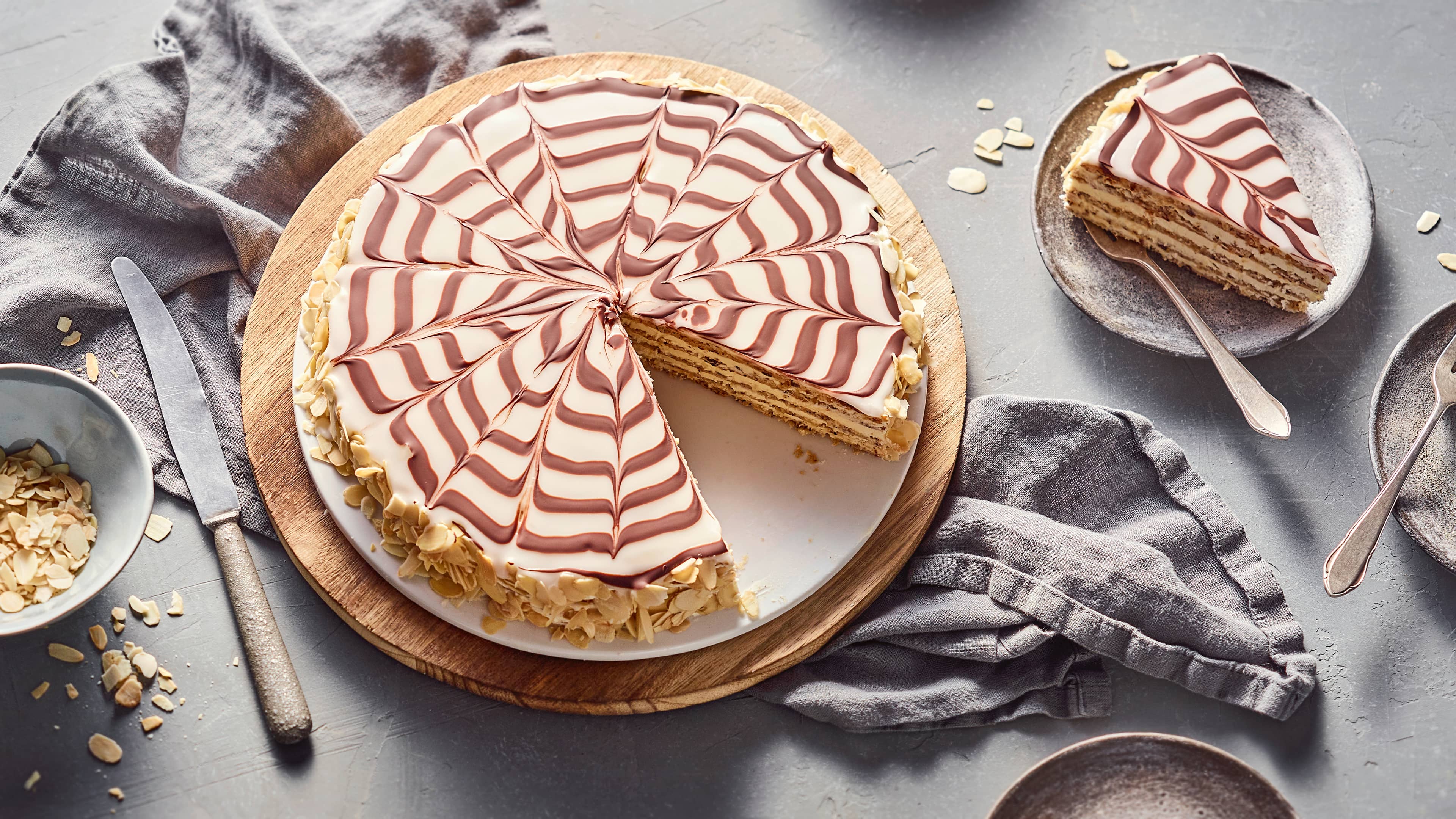Rezept für die ungarische Esterházy-Torte Eine Creme-Torte mit einem Rand aus Haselnüssen, glasiert mit weißem Zuckerguss mit Schokoladenspinnennetz-Muster