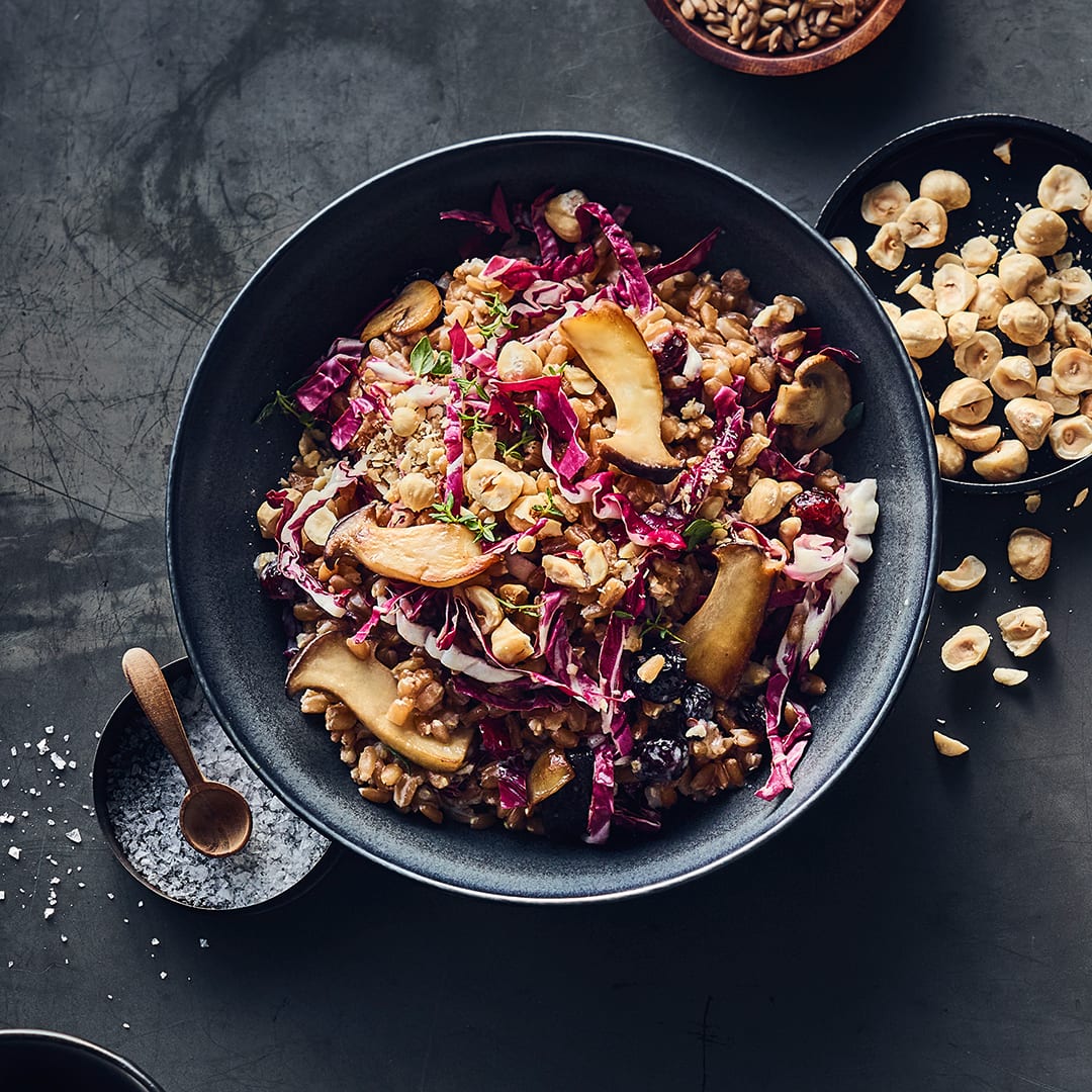 Eine Keramikschüssel, befüllt mit Dinkel-Risotto mit Radichio und Kräuterseitlingen, getoppt mit blanchierten Haselnüssen