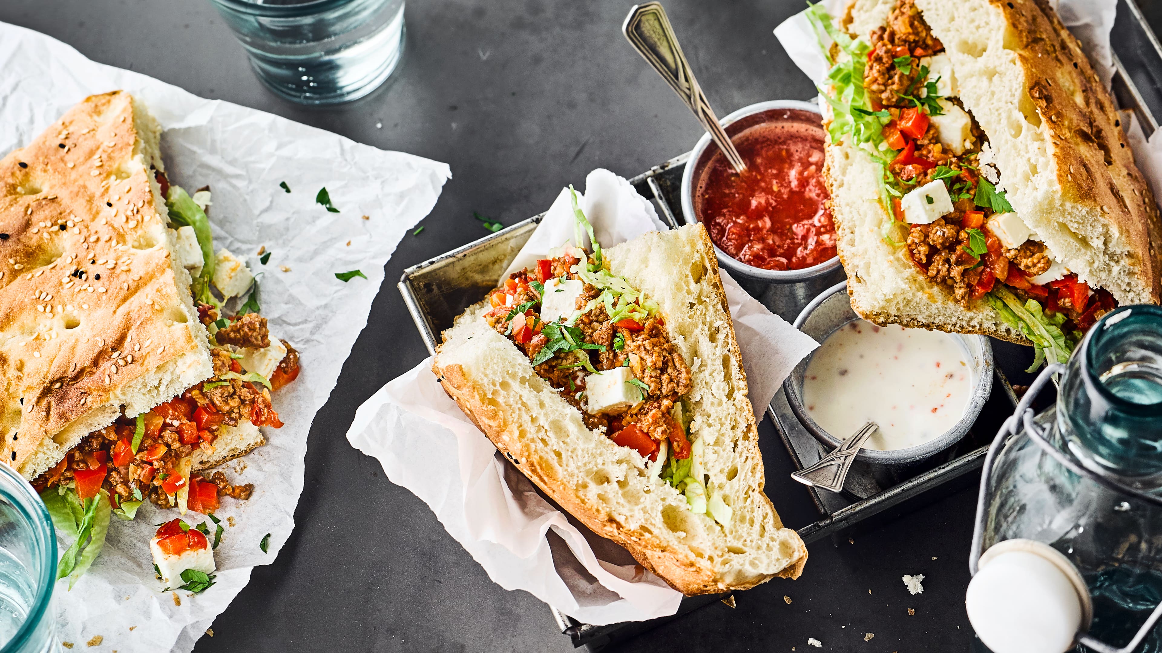 Rezept für Fladenbrot mit Hackfleisch Fladenbrote mit Hackfleisch, Paprika, Tomaten, Feta und Petersilie sowie eine rote und helle Sauce in einer Metallbox