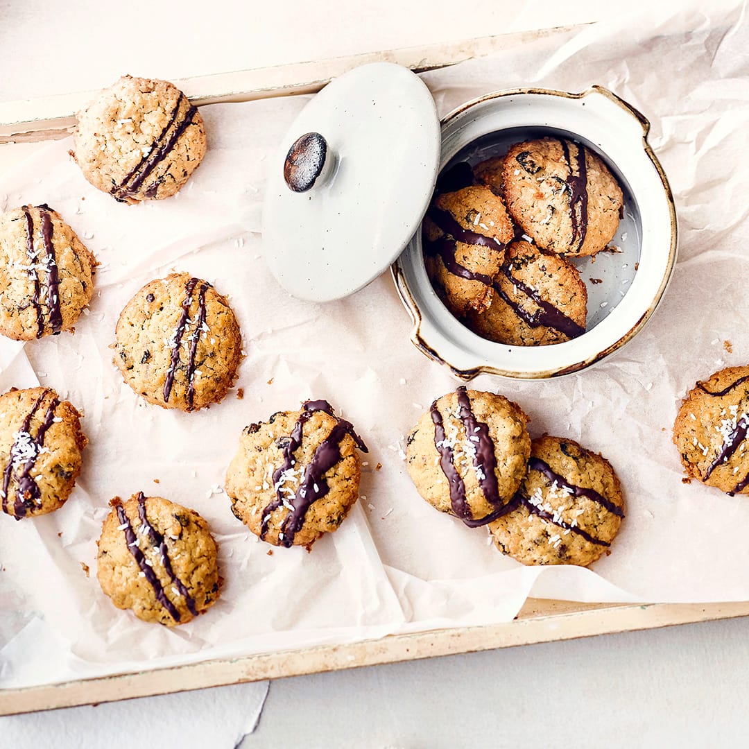 Diese leckeren Kekse schmecken nicht nur zur Weihnachtszeit: Probieren Sie unser fruchtigen Cookies aus Weizenmehl, Butter, Zucker und Kokosraspeln – mit getrockneten Cranberrys und verziert mit dunkler Kuchenglasur!