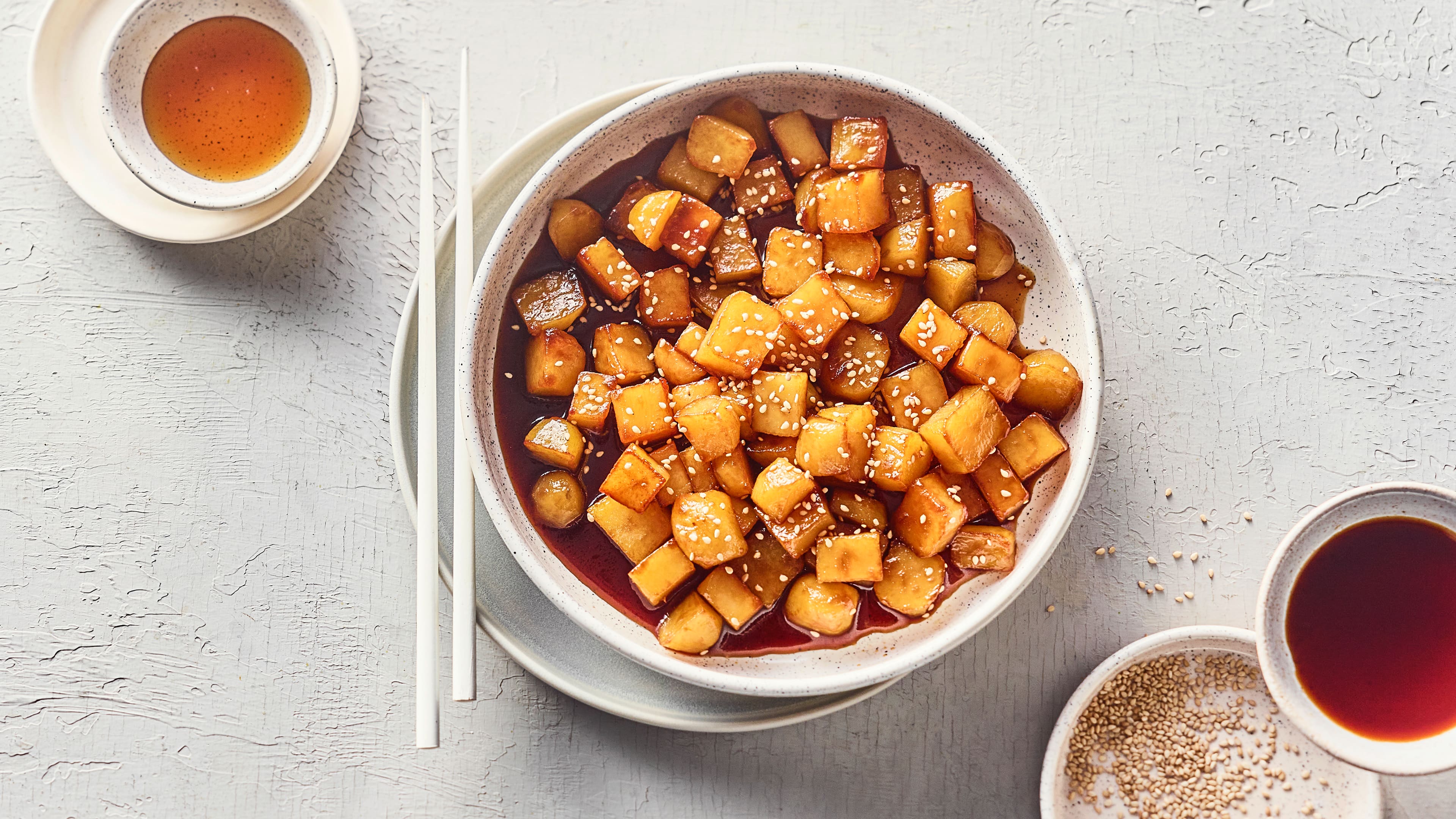 Ein tiefer Teller mit Kartoffelwürfeln in einer klaren rotbraunen Sauce, getoppt mit Sesam
