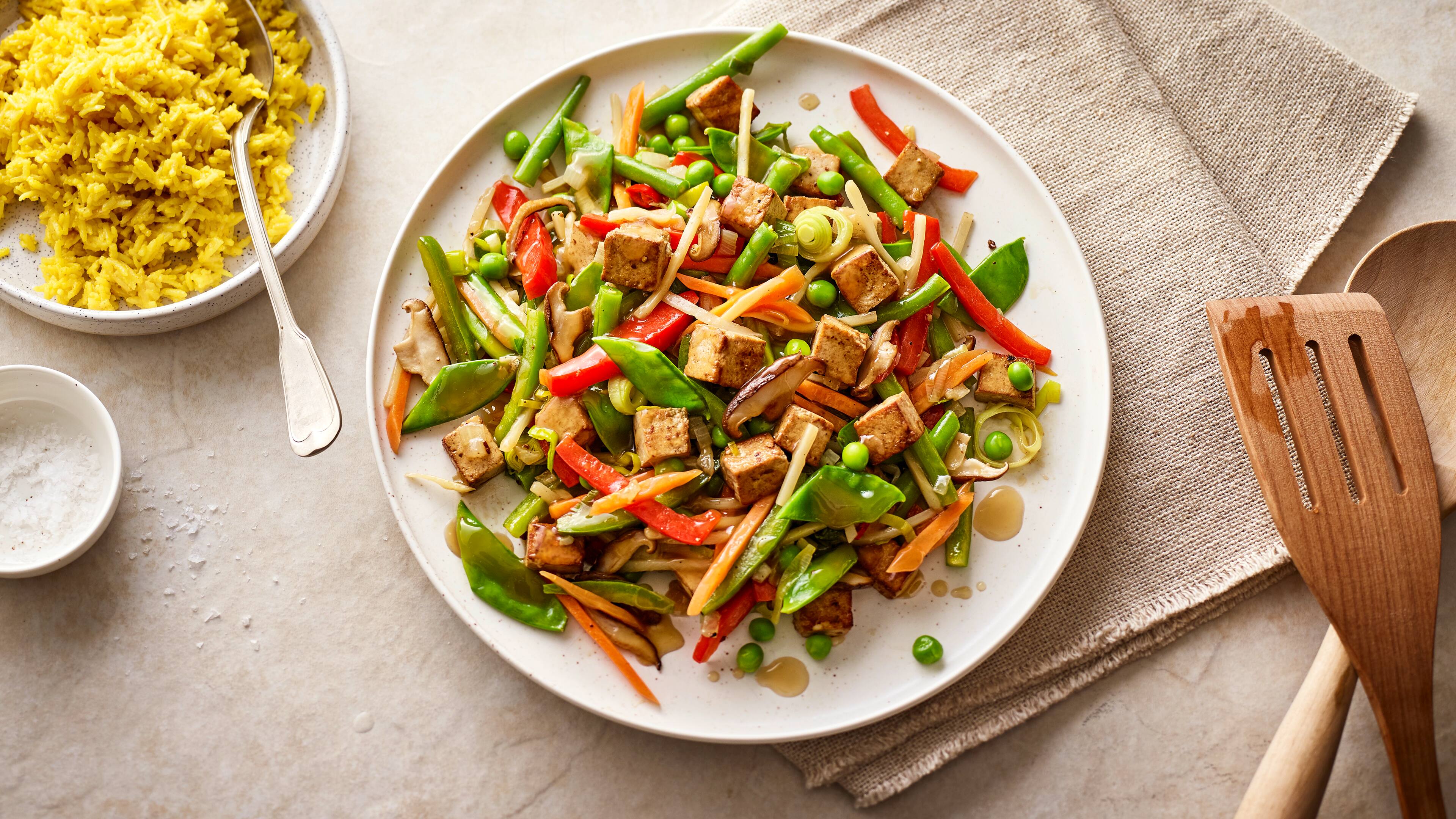 Rezept für gebratenes Gemüse mit Tofu Ein runder Teller mit gebratenen Möhren, Paprika, Pilzen, Zuckerschoten, Erbsen, Lauch und knusprigem Tofu