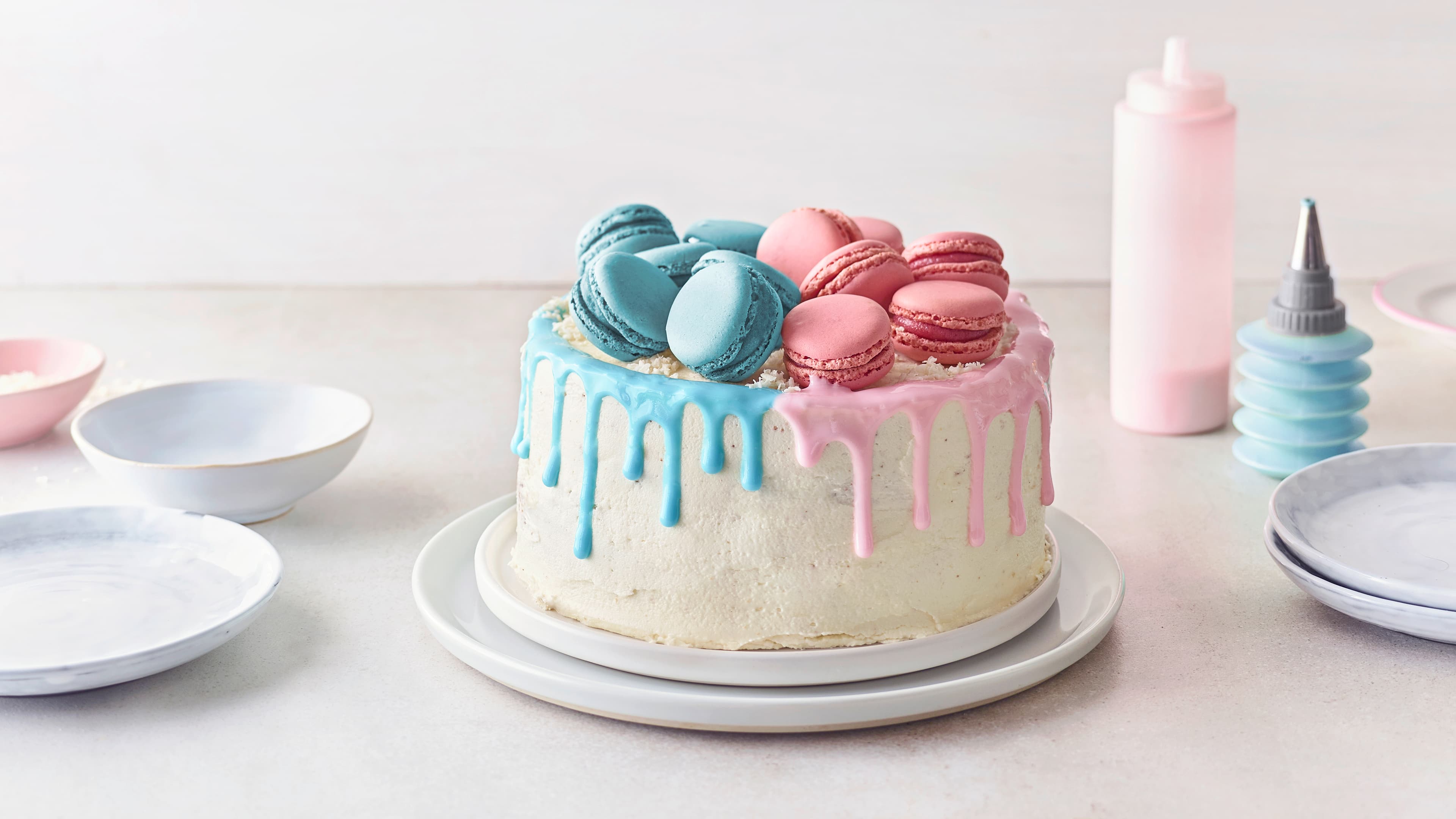 Rezept für Gender Reveal Cake Eine Creme-Torte, dekoriert mit Schoko-Drip und Macarons, auf einer Hälfte in rosa und der anderen hellblau, auf einem Teller