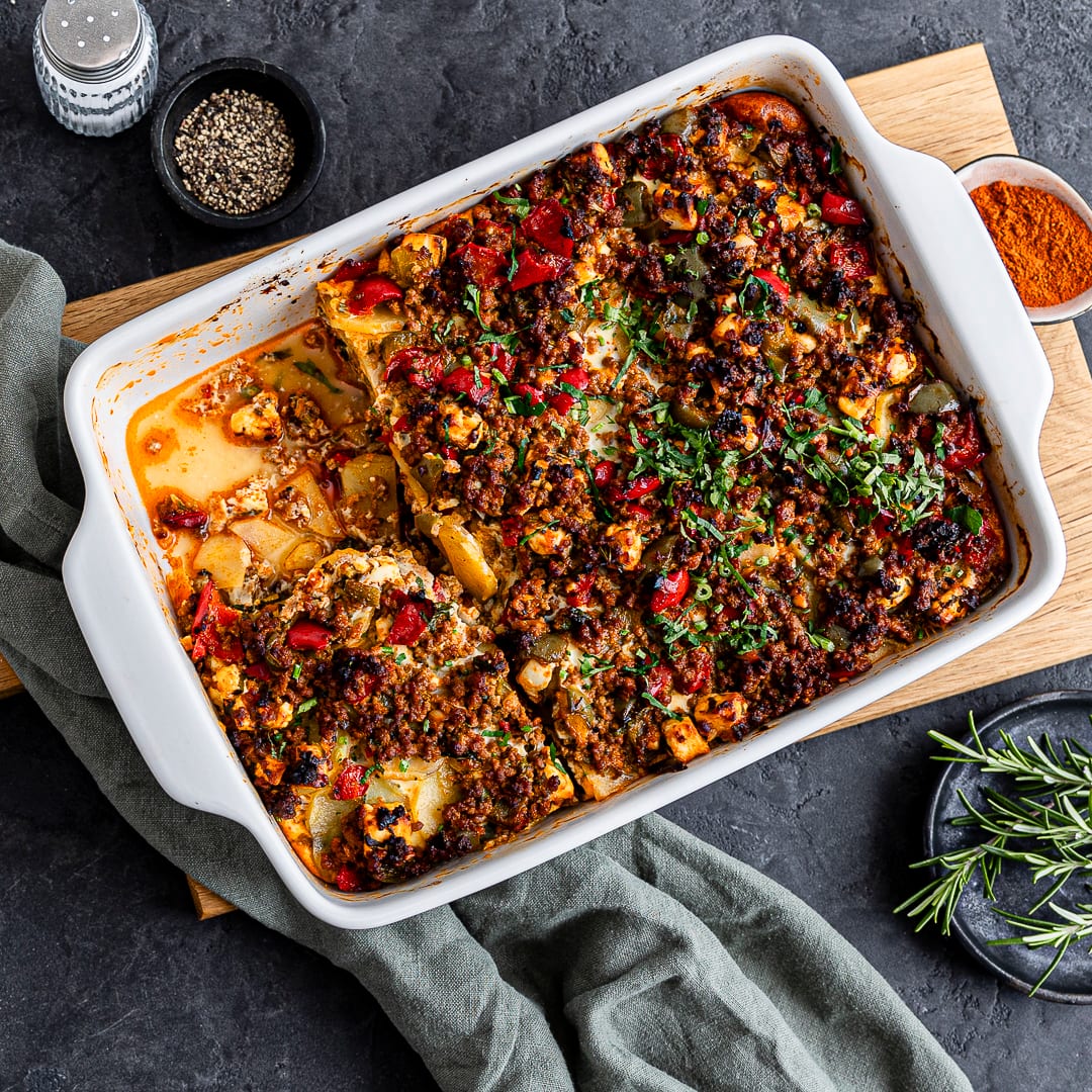 Eine Auflaufform mit überbackenen Kartoffelstückchen, Hackfleisch und Paprika, getoppt mit  Petersilie und Rosmarin