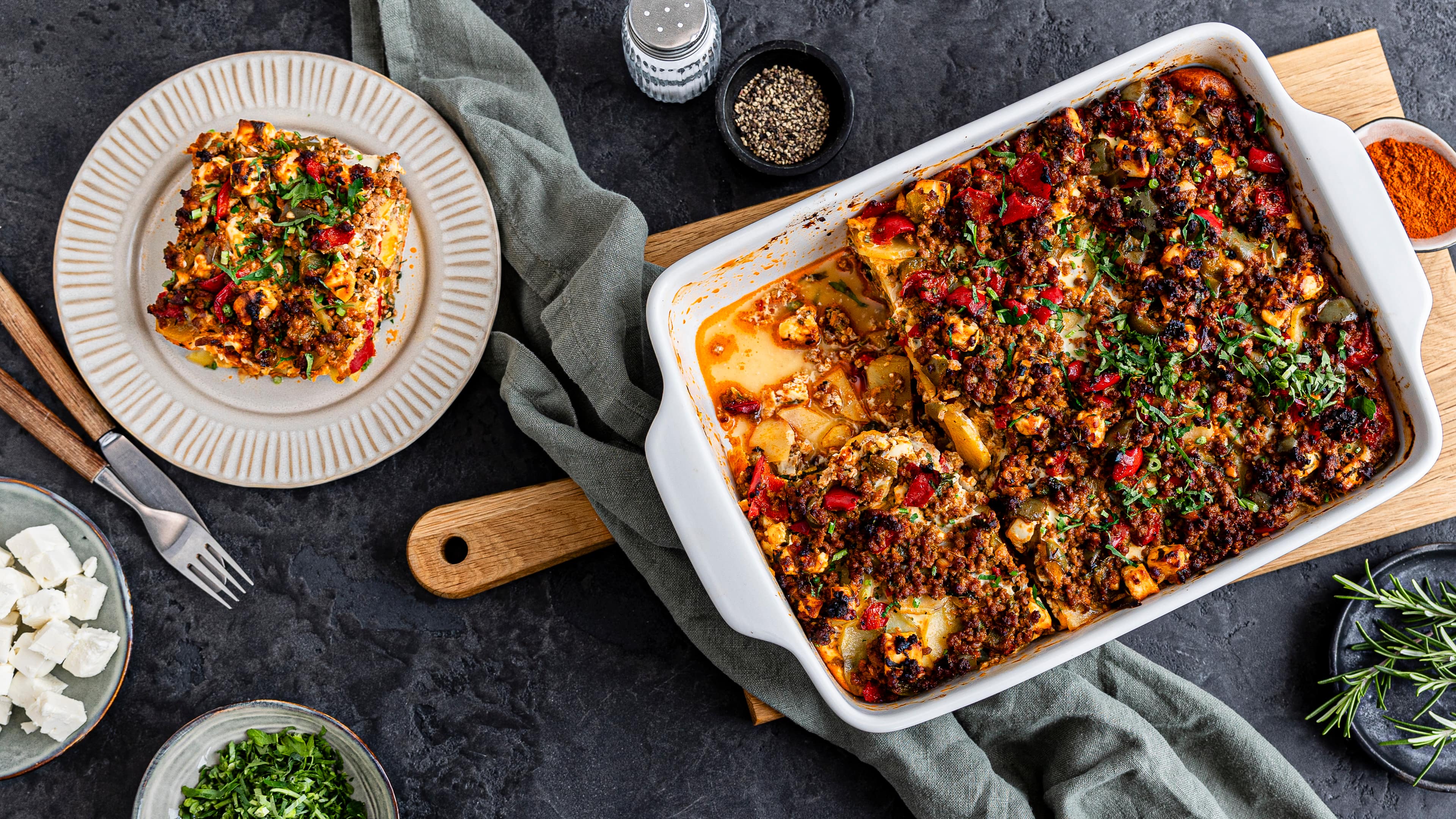 Rezept für Hackfleisch-Auflauf mit Kartoffeln Eine Auflaufform mit überbackenen Kartoffelstückchen, Hackfleisch und Paprika, getoppt mit Petersilie und Rosmarin