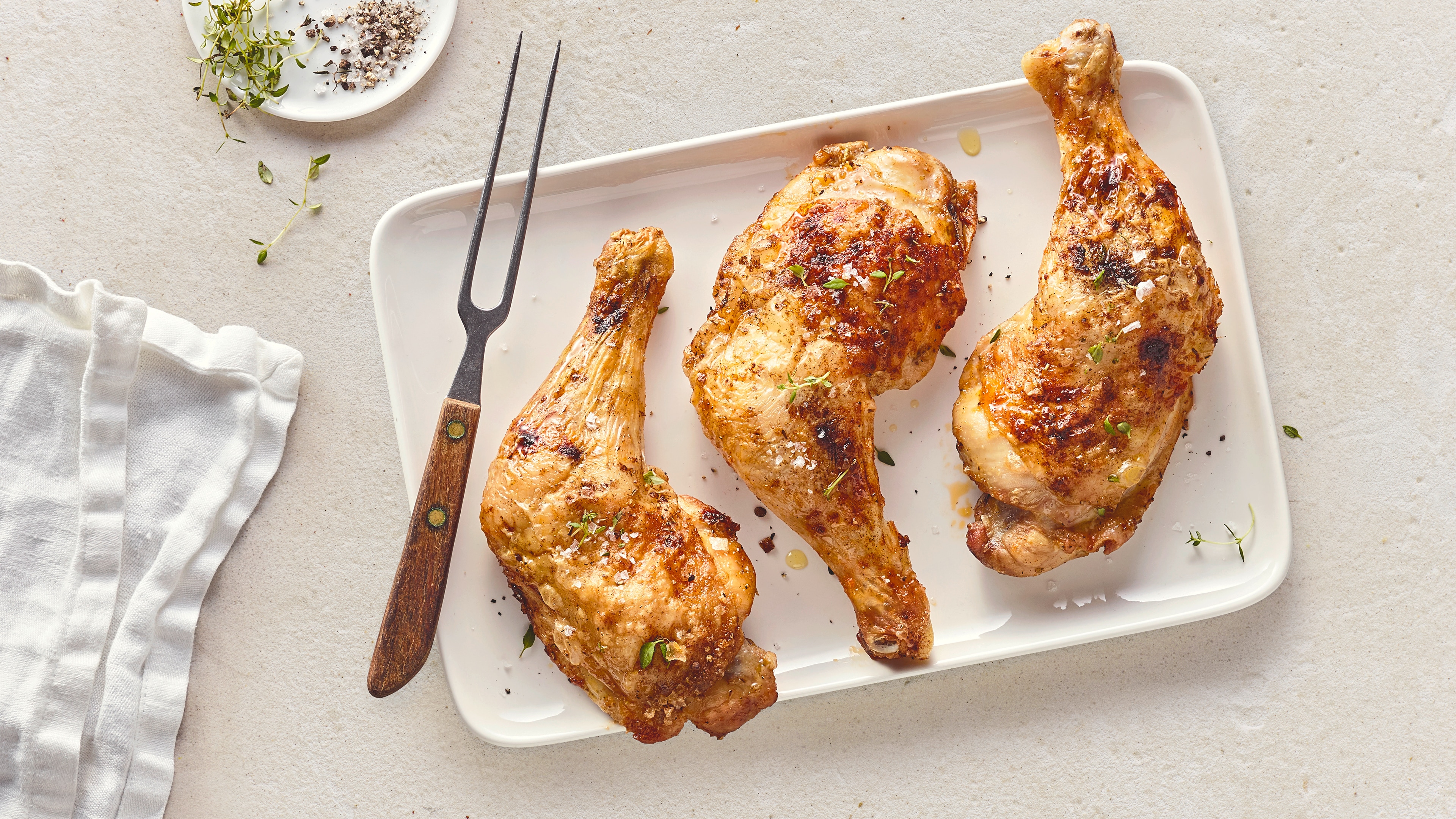 Rezept für Hähnchenschenkel aus der Heißluftfritteuse Hähnchenschenkel mit einer knusprigen Kruste, getoppt mit etwas frischem Thymian, auf einer Keramikplatte