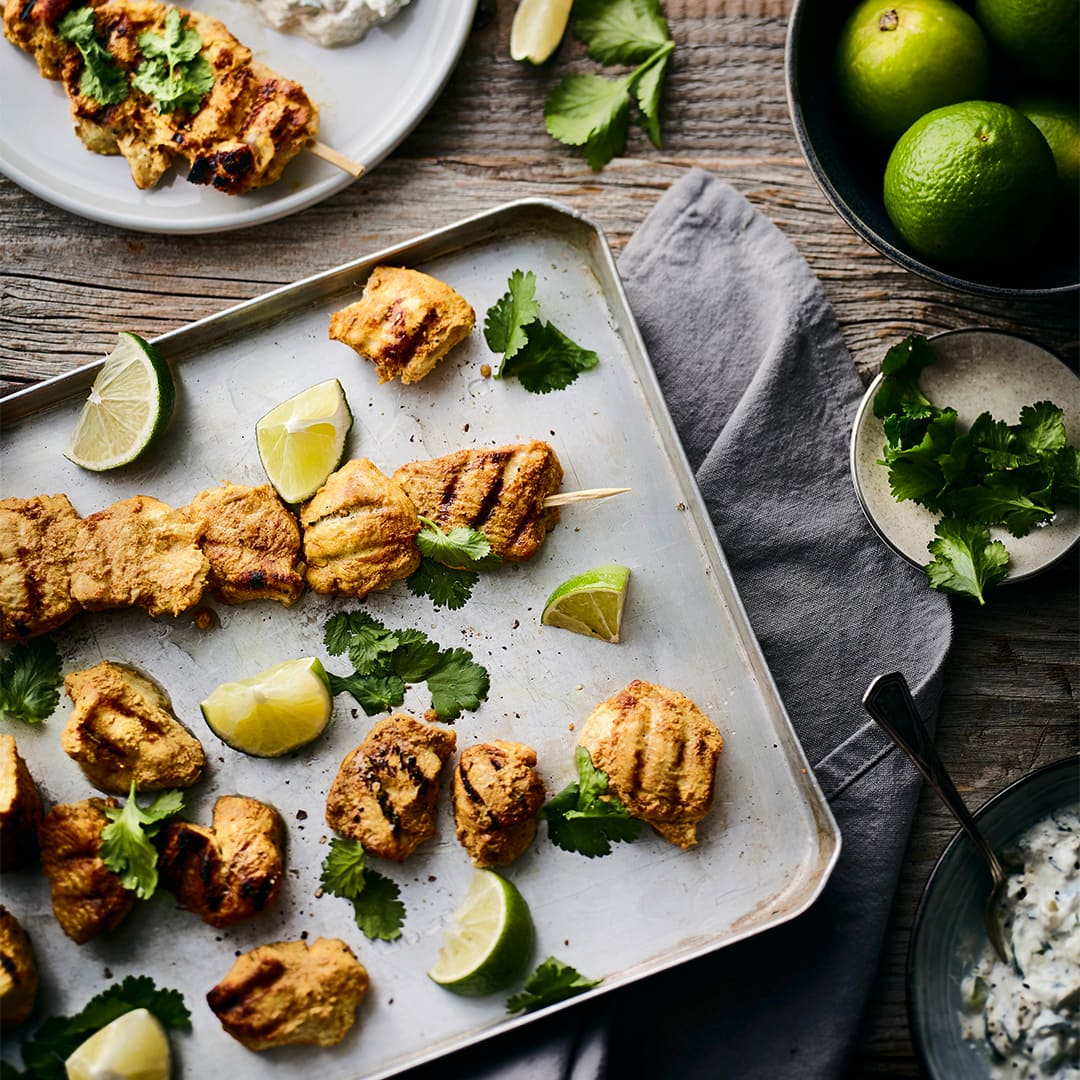 Allerlei Gewürze sowie frische Limetten geben den Hähnchenspießen vom Grill die köstliche Würze. Dazu passt Raita, ein indischer Joghurt-Dip.