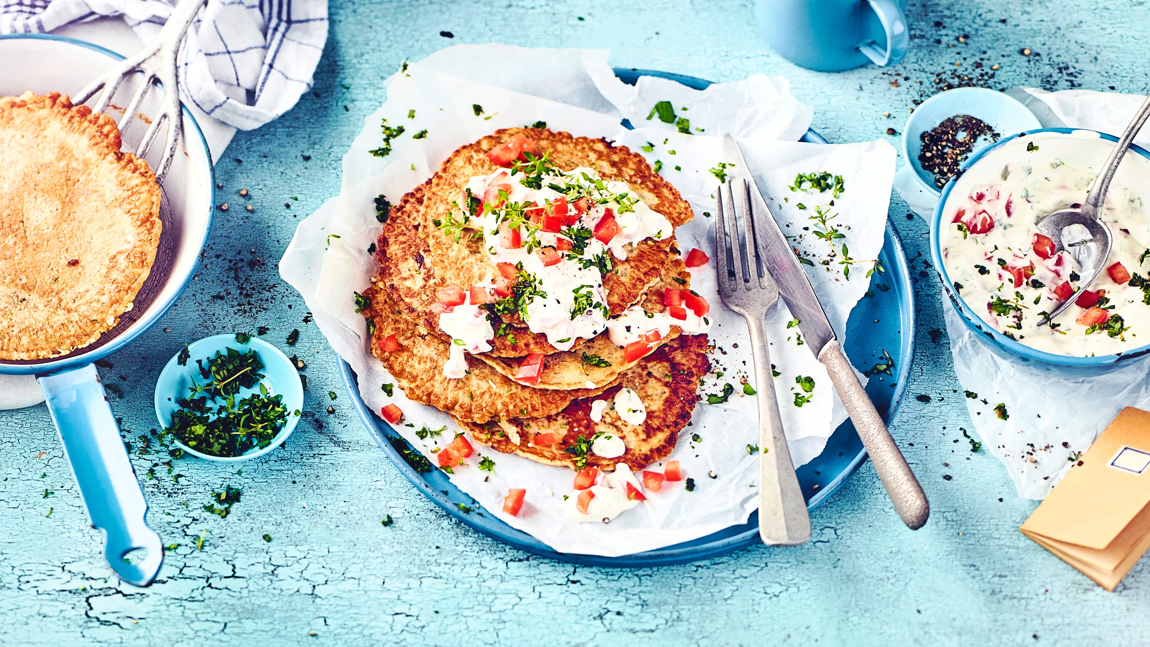 Ein Teller mit gelbgoldenen Pfannkuchen mit Quark-Joghurt-Dip, Tomaten und frischen Kräutern
