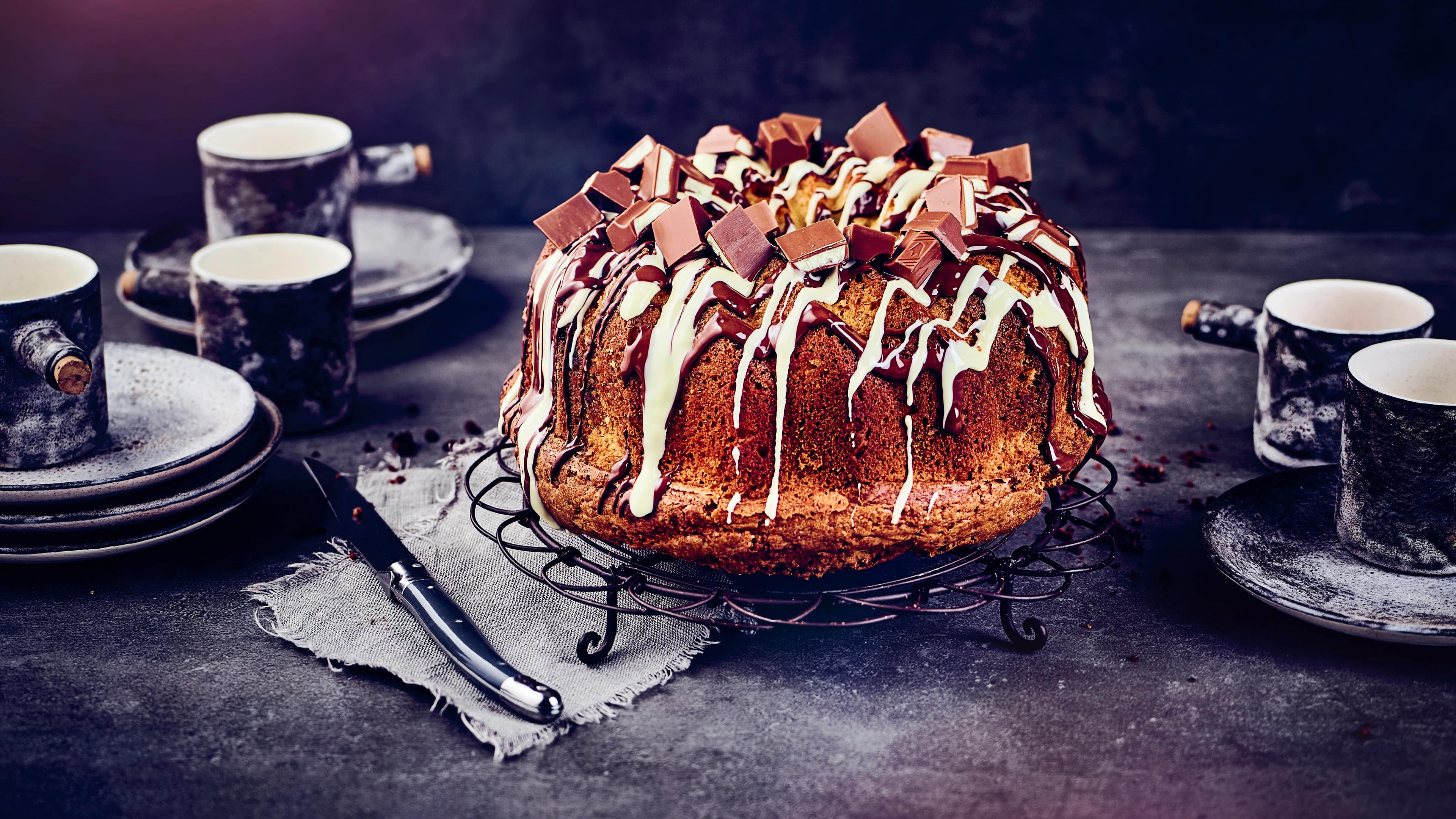 Rezept für Kinder-Schokolade-Kuchen Ein Gugelhupf, getoppt mit weißer und dunkler Kuvertüre sowie Stückchen Kinderschokolade, auf einem Kuchengitter