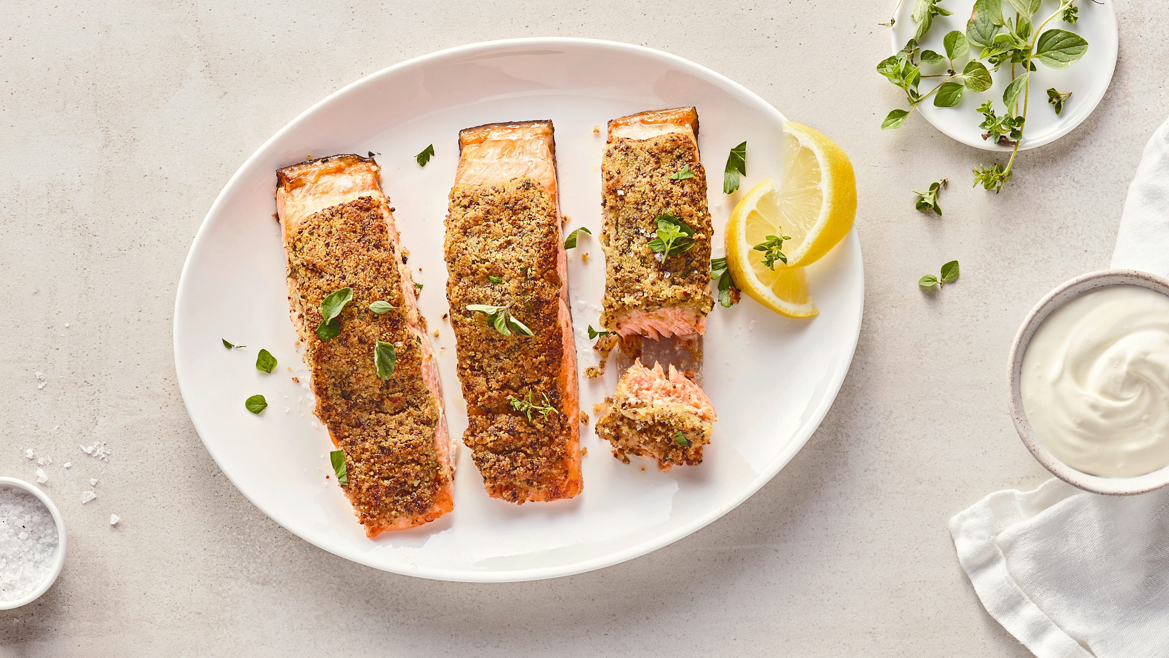 Rezept für Lachs aus dem Airfryer Drei Lachsstücke mit einer Kruste, auf einem ovalen Teller, getoppt mit frischer Petersilie und Zitronenspalten