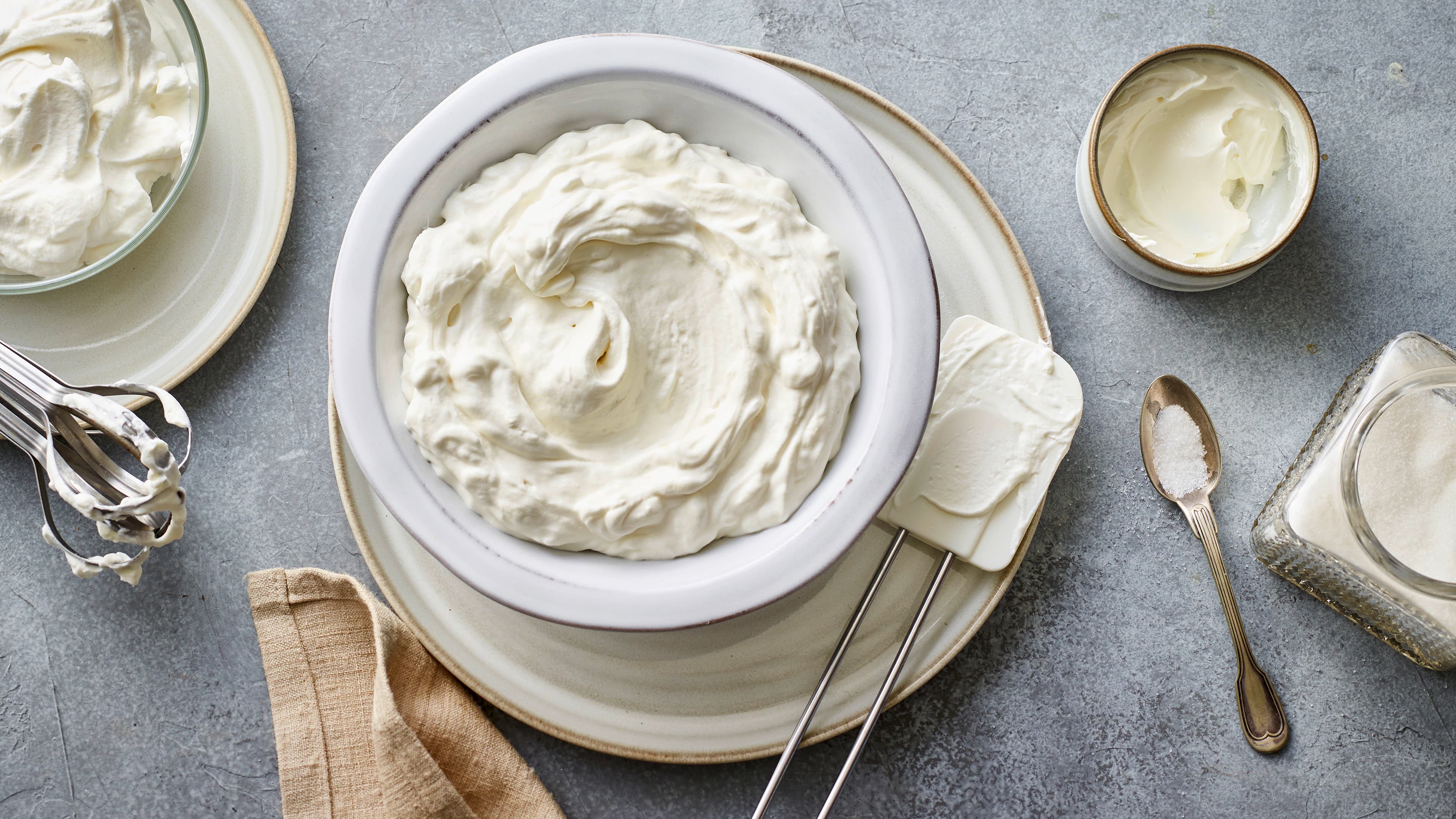 Rezept für Mascarpone-Creme Eine Schale mit luftiger, homogener heller Creme, daneben ein Silikon-Spachtel