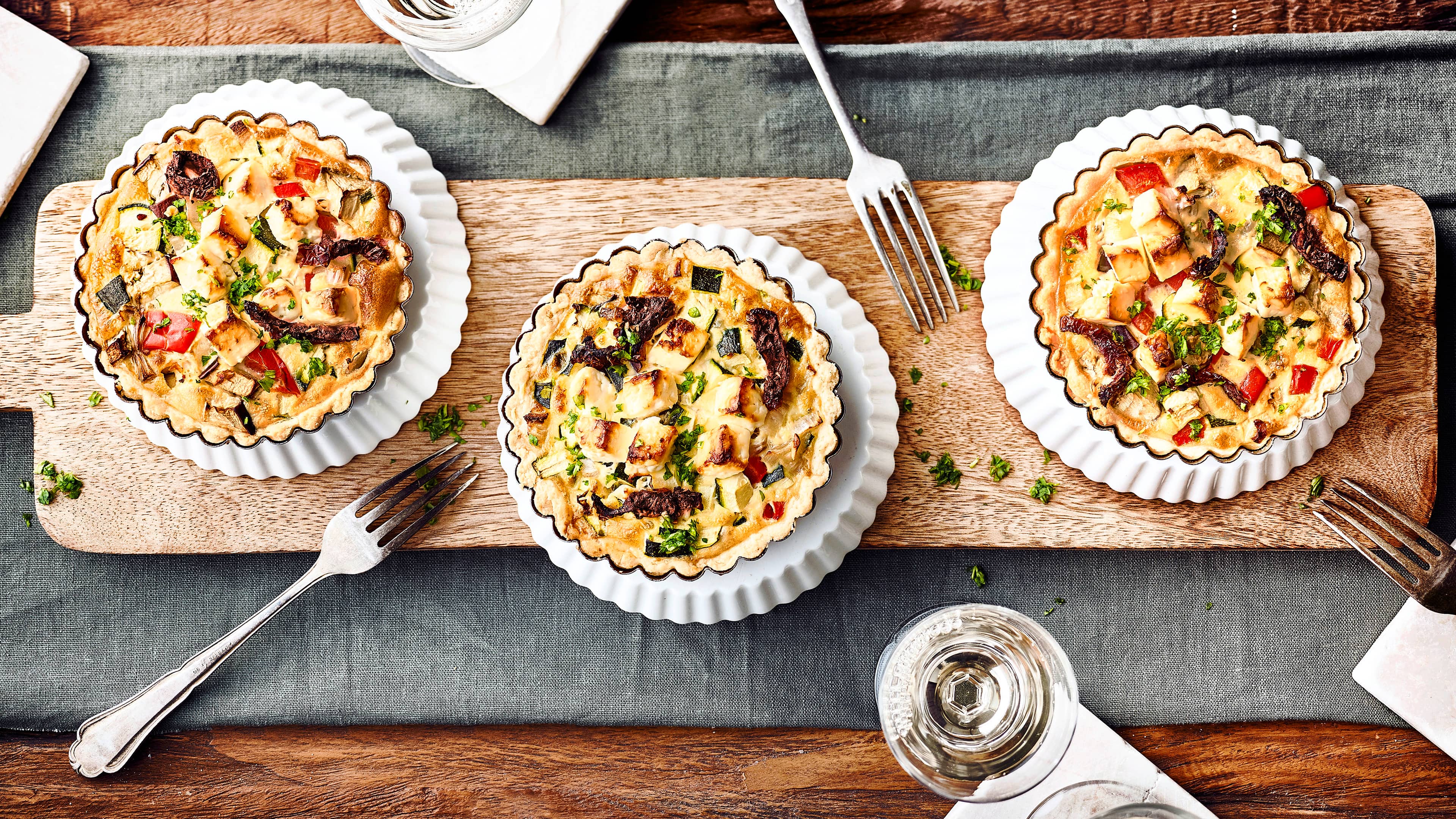 Mediterrane Gemüsetarteletts Mediterraner Snack für zuhause: Kleine selbstgemachte Mürbeteig-Törtchen mit allerlei mediterranem Gemüse und Feta.