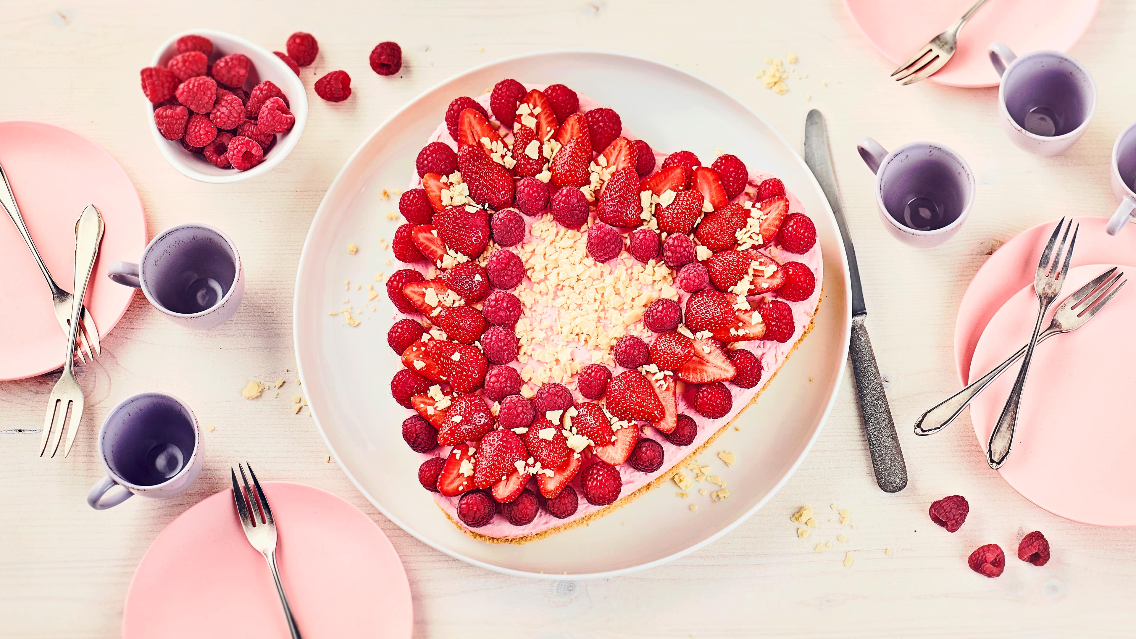 Muttertagsherz Luftiger Biskuit, gefüllt mit einer köstlichen Erdbeer-Vanillecreme mit Erdbeerlikör und anschließend mit Erdbeeren, Himbeeren und weißer Schokolade dekoriert.