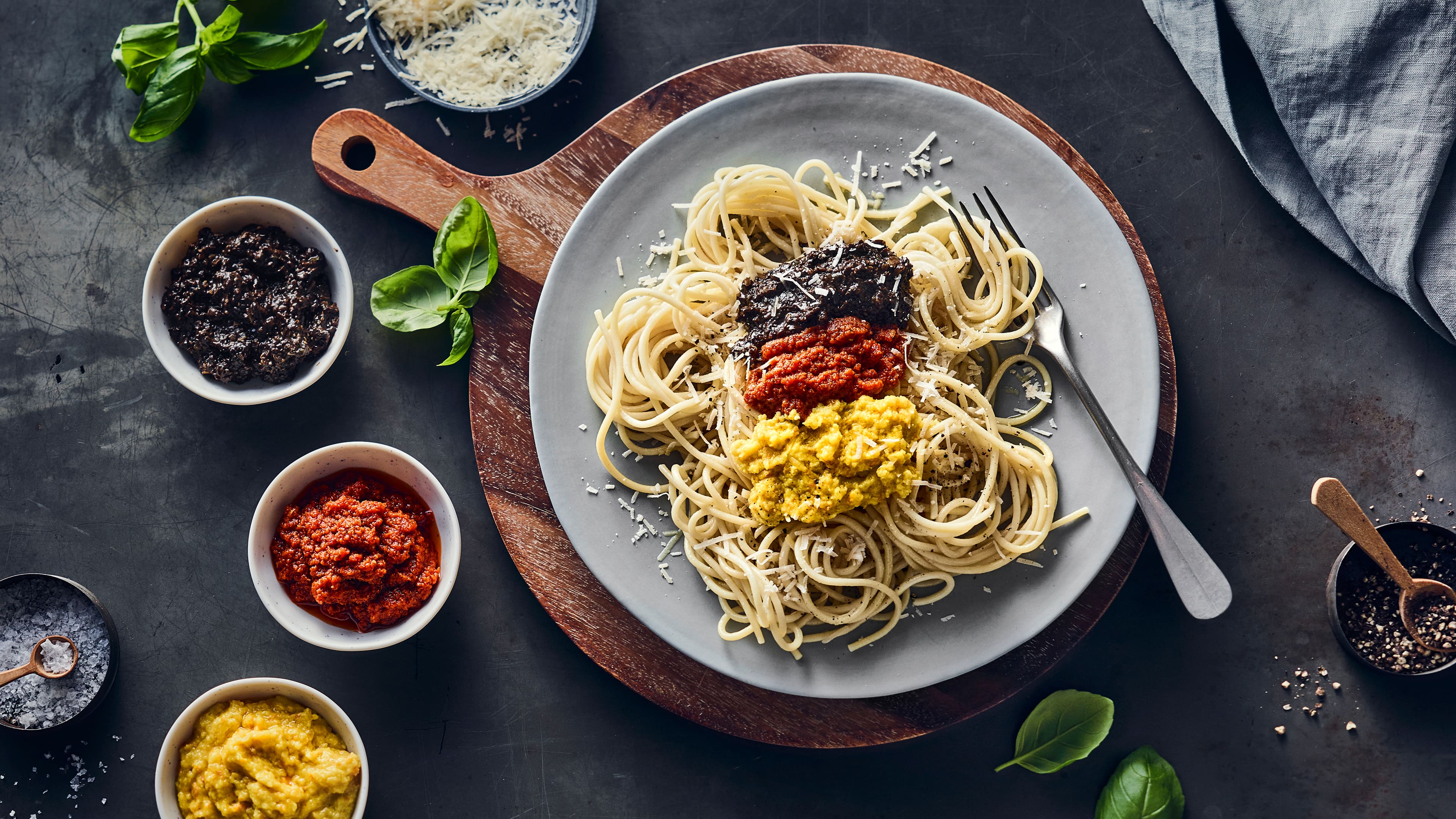 Ein runder Teller mit Spaghetti, getoppt mit schwarzen, roten und gelben Pesto sowie Parmesan