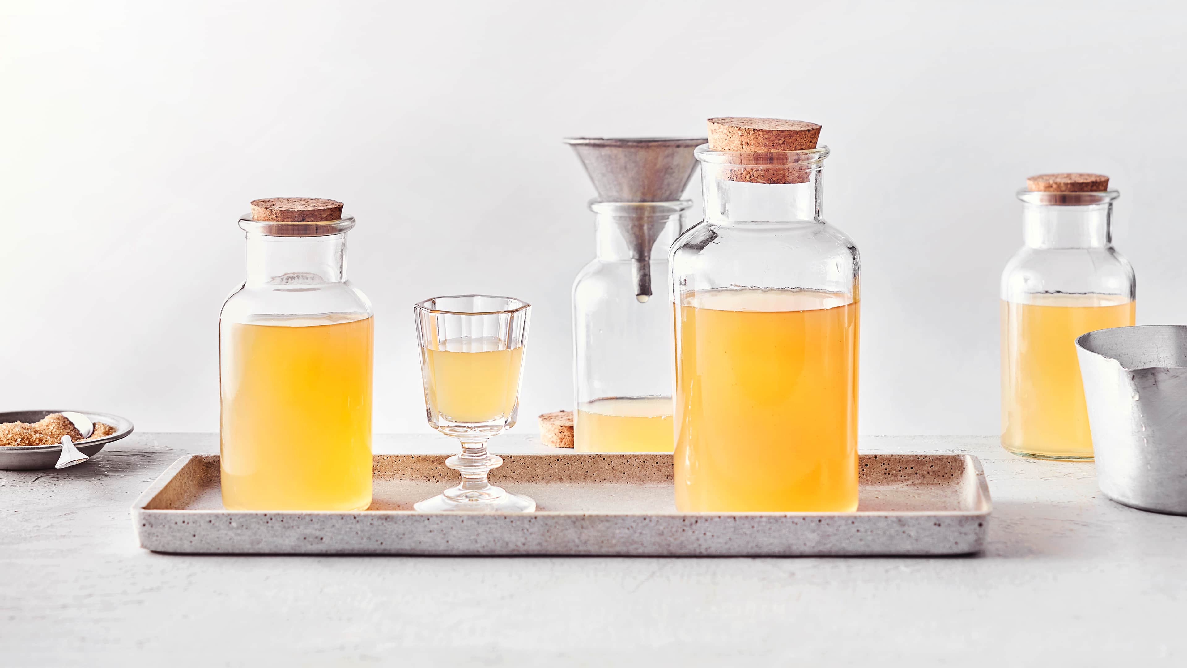 Rezept für selbst gemachten Pfirsichlikör Zwei verschlossene Flaschen mit Korken und ein eckiges Trinkglas, befüllt mit orange-gelbem klarem Likör