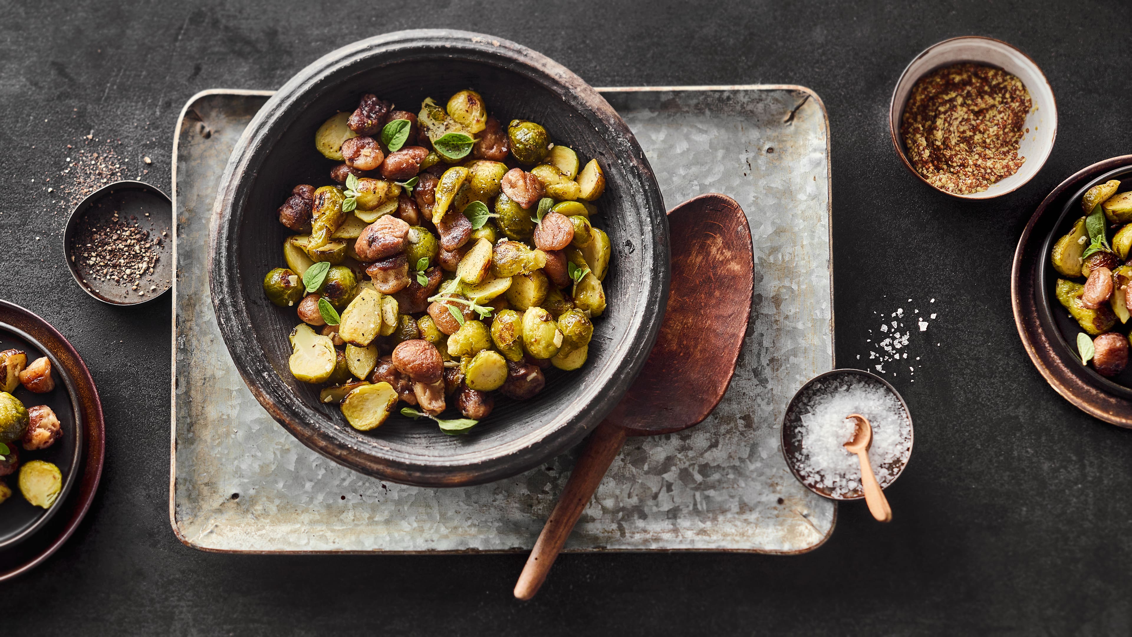 Rezept für gerösteten Rosenkohl mit Maronen Gerösteter Rosenkohl und Maronen, serviert in einer rustikalen Schüssel, daneben ein großer Salatlöffel aus dunklem Holz