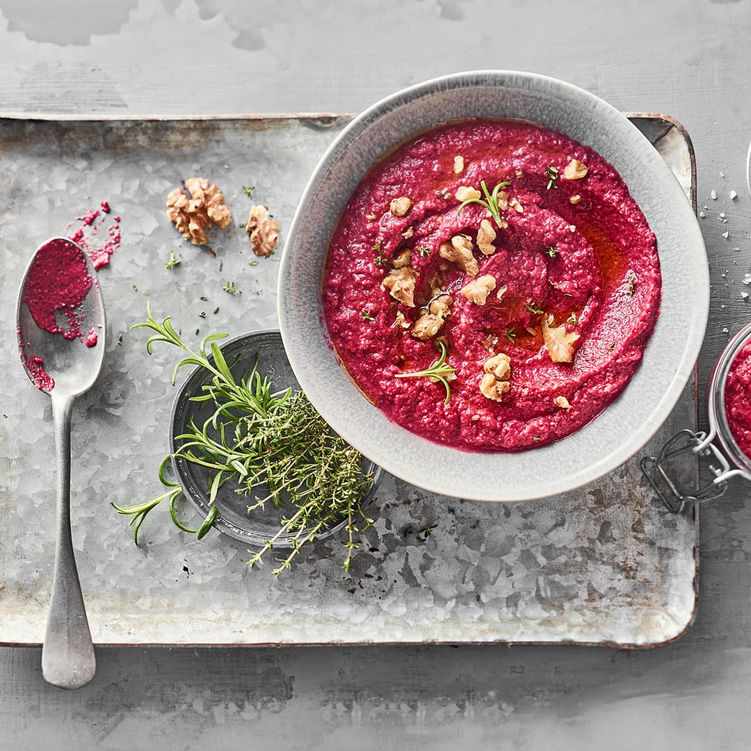 Auf einem Metallblech eine kleine Schüssel gefüllt mit pinkem cremigem Pesto, das mit Walnusskernen garniert ist