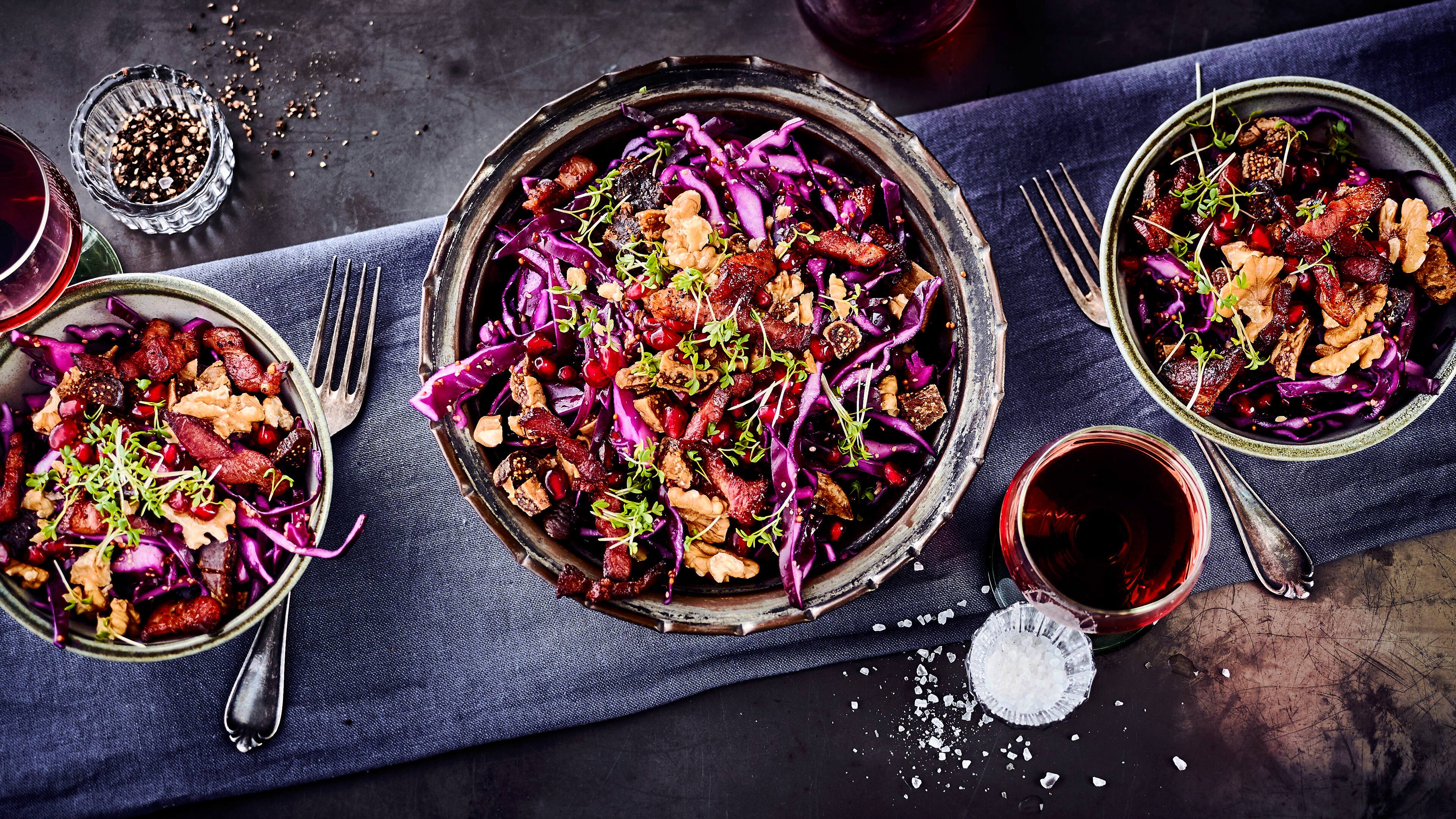 Rezept für Rotkohlsalat mit Granatapfelkernen und Walnüssen Drei Schüsseln mit einem Salat aus Rotkohl, getoppt mit Walnüssen, Filetstücken, Kresse und Granatapfelkernen
