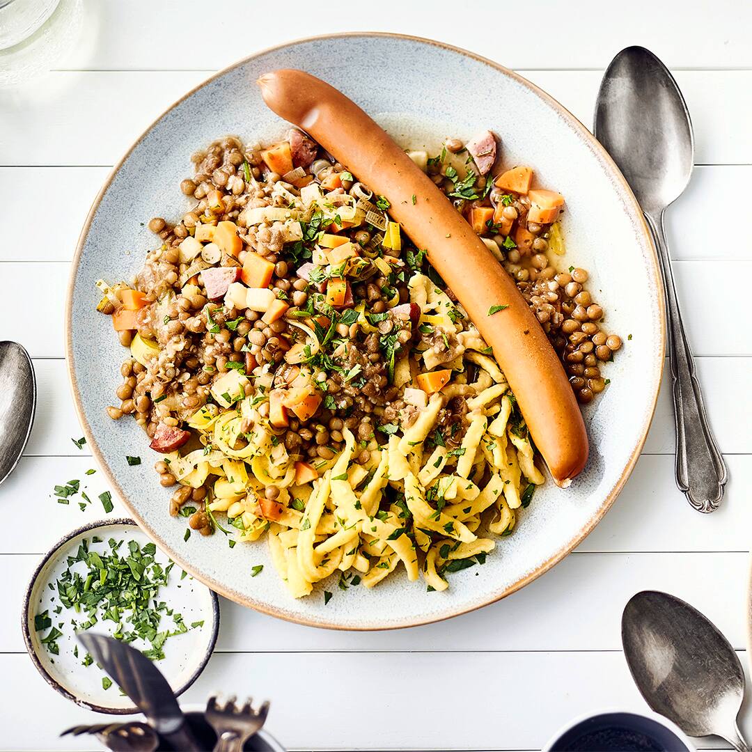 Deftiger Eintopf für Eilige: Servieren Sie mit unserem Rezept einen schnellen Linseneintopf mit Cabanossi und Kräuterspätzle – in nur 30 Minuten!