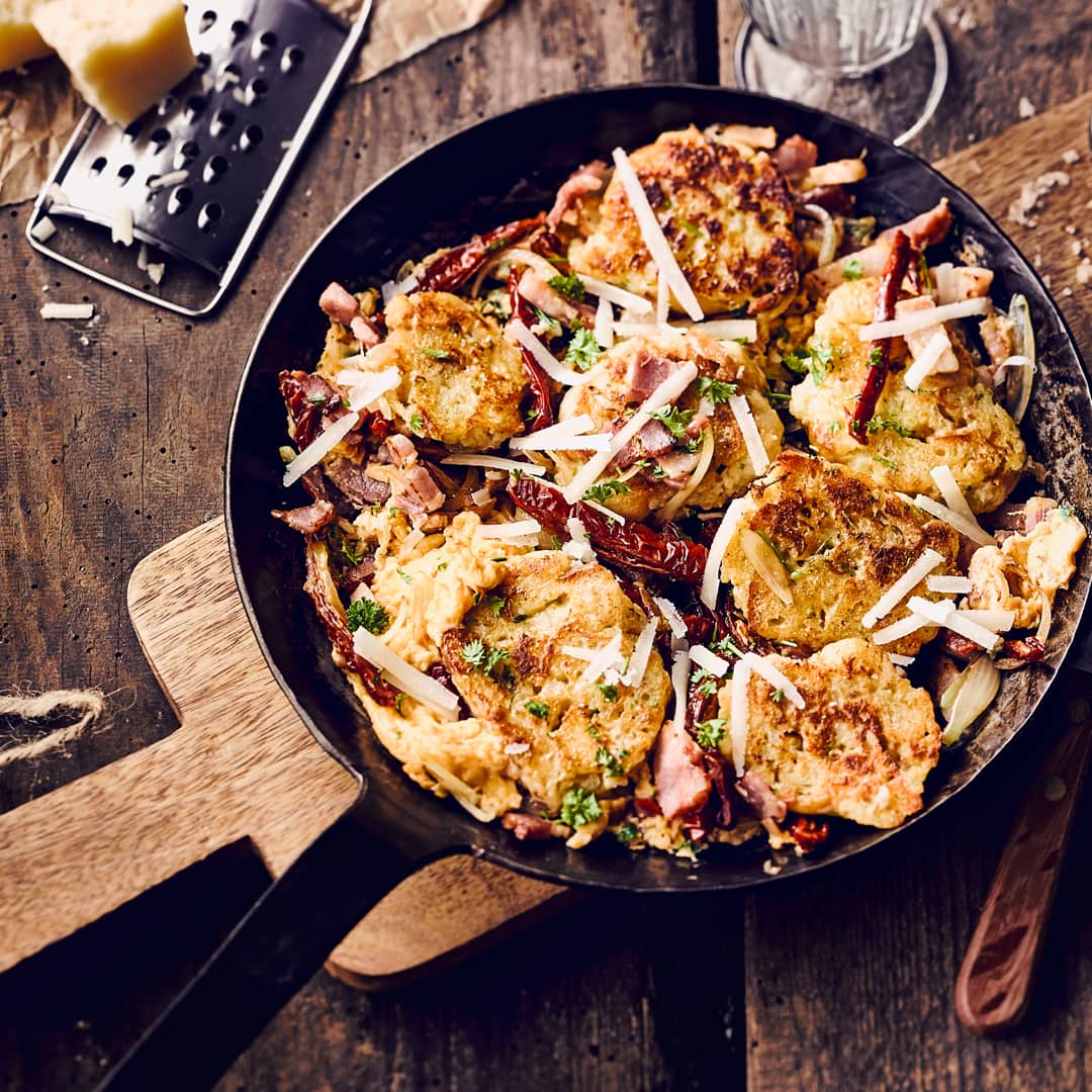 Eine Pfanne mit Teigknödeln, geräuchertem Speck, getoppt mit geriebenem Käse und gehackter Petersilie