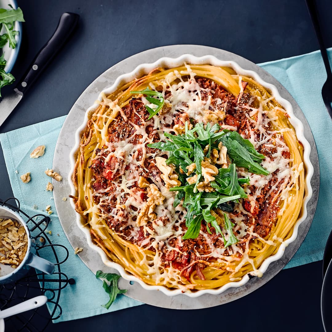 Pasta einmal anders: Verwöhnen Sie Ihre Familie mit unserer Spaghetti-Tarte – gefüllt mit Rinderhack, Mozzarella, Sahne und Karotten, garniert mit frischem Rucola und gehackten Walnüssen!
