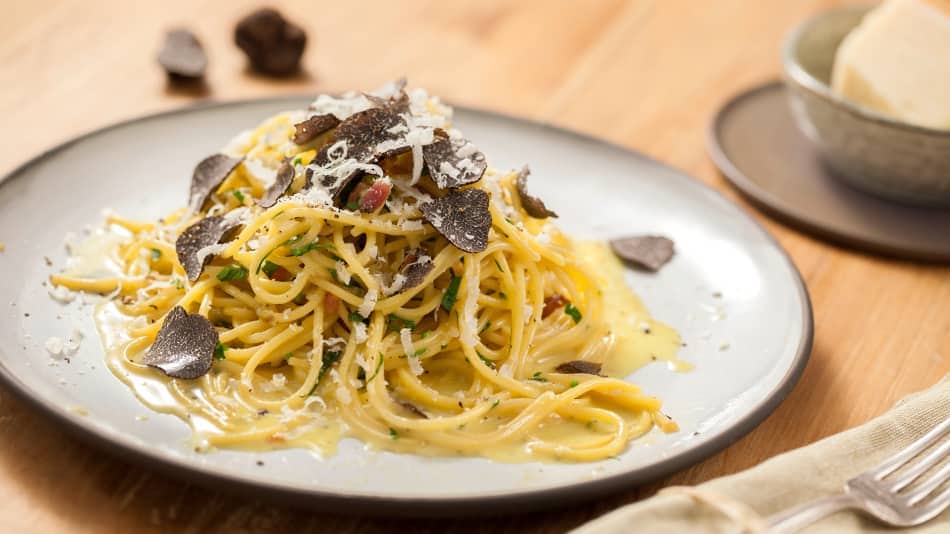 Rezept für Trüffel-Pasta Ein Teller mit Spaghetti in cremig-buttriger Sauce, getoppt mit geriebenem Parmesan, gehobeltem Trüffel und Speckwürfeln