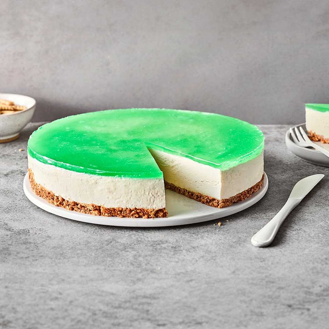 Runde Frischkäsetorte mit einem Boden aus Butterkeks und einer grünen Waldmeister-Wackelpuddingschicht auf einem Teller