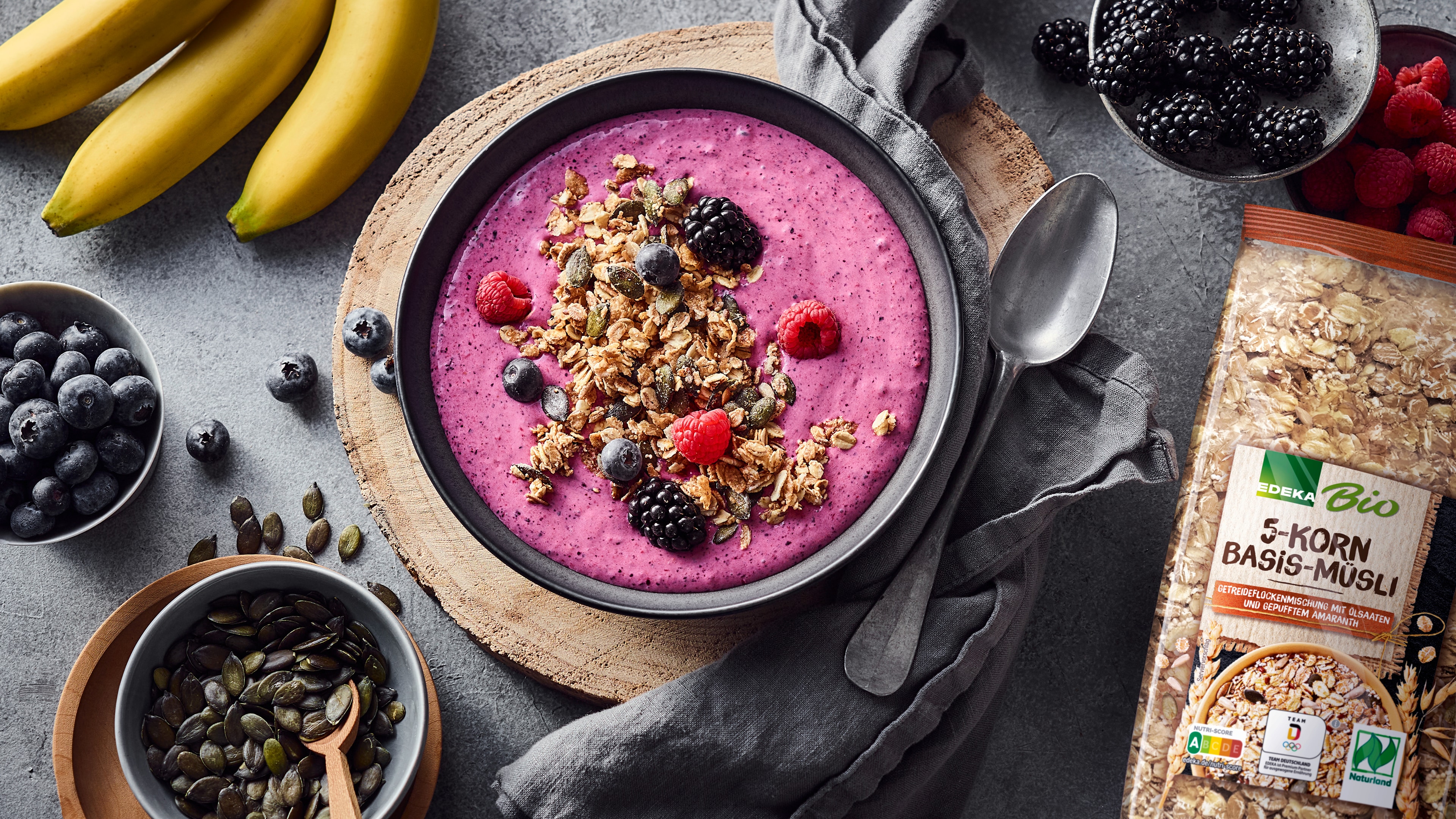 Eine Schüssel mit pinker, cremiger Flüssigkeit, garniert mit Waldbeeren, Kürbiskernen und Fünfkornflocken