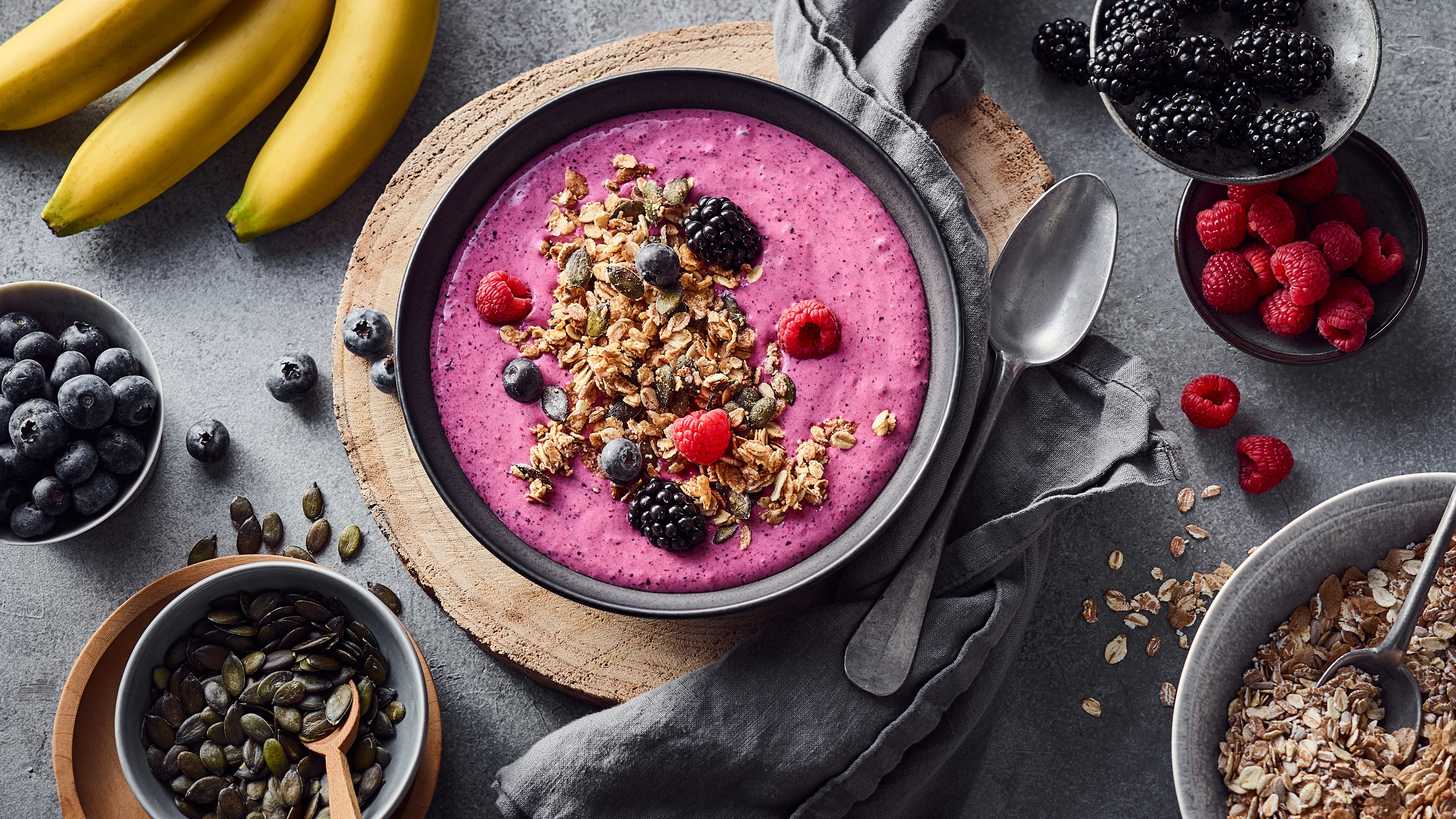 Eine Schüssel mit pinker, cremiger Flüssigkeit, garniert mit Waldbeeren, Kürbiskernen und Fünfkornflocken