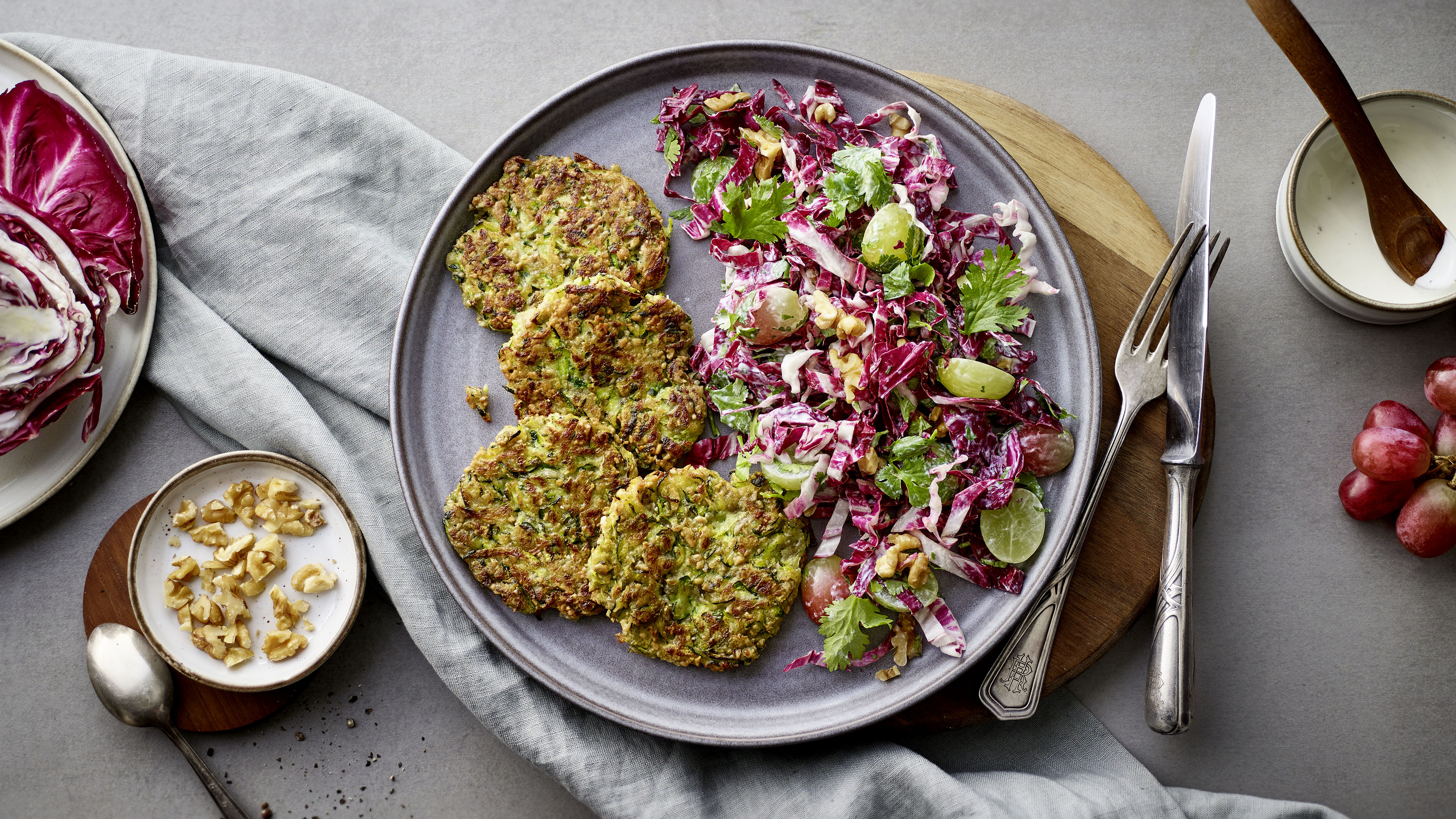 Knusprige Gemüsebratlinge mit Radicchio-Trauben-Salat und Walnüssen auf einem Teller, serviert mit cremigem Dressing auf grauem Hintergrund.