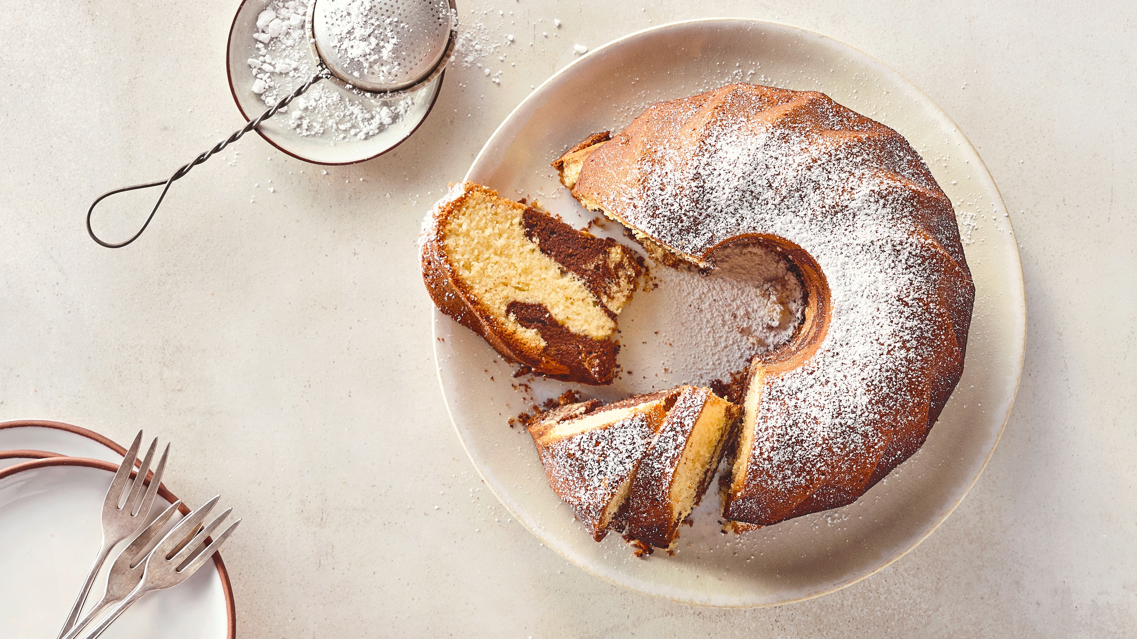 Ein Teller mit Rührkuchen aus hellem und dunklem Teig mit einem marmorartigen Muster, bestreut mit feinem Puderzucker