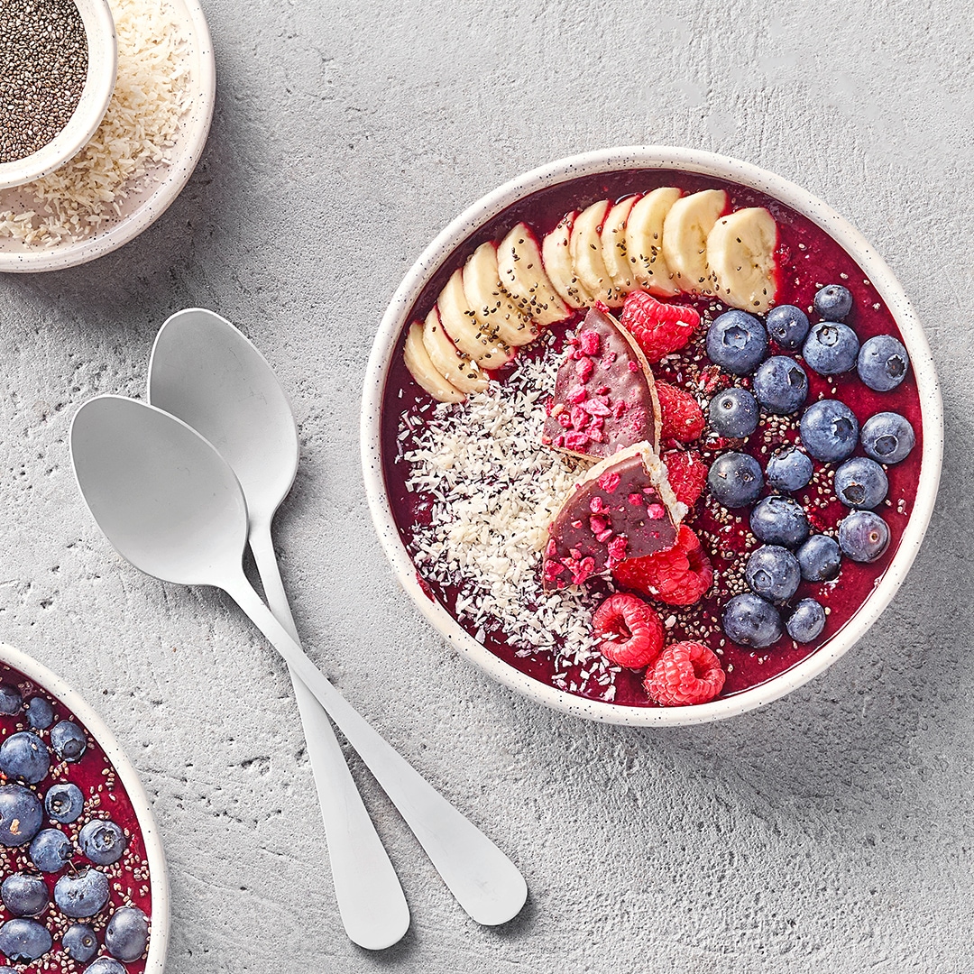 Große Schale mit roter Creme, Bananenscheiben, Heidelbeeren, Himbeeren und Kokosraspeln