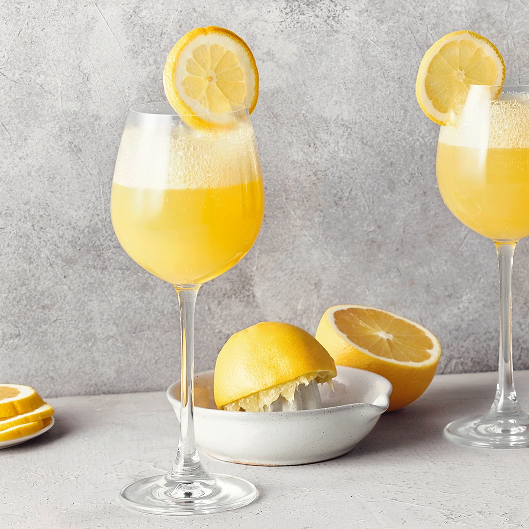 Ein Glas mit gelbem Zitronensaft, garniert mit einer dünnen Zitronenscheibe am Rand