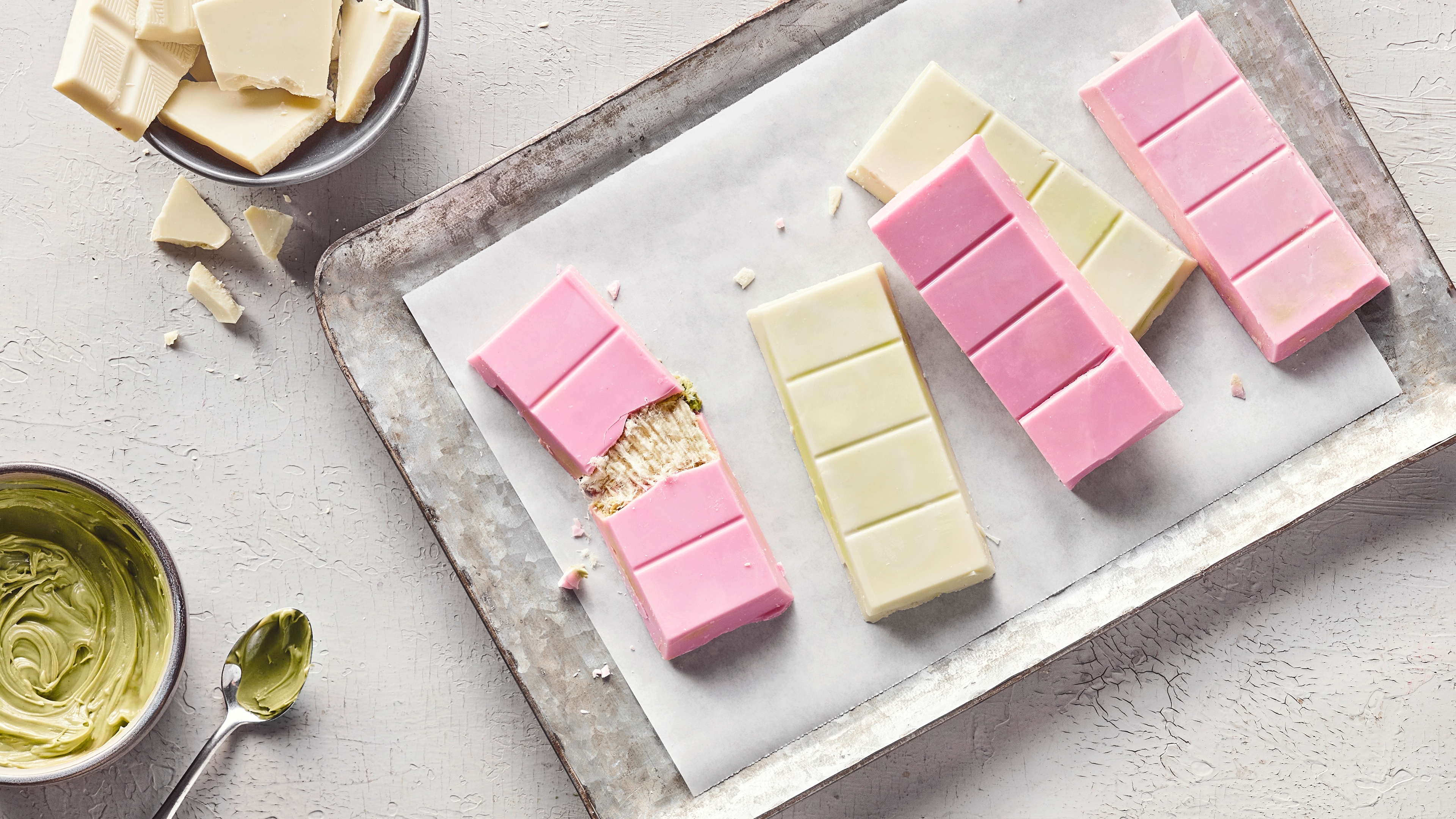 Rezept für Angel Hair Schokolade Längliche Tafeln weiße und pastellrosa Schokolade, gefüllt mit einer hellen, fädigen Creme, daneben ein Löffel mit Pistazienmus
