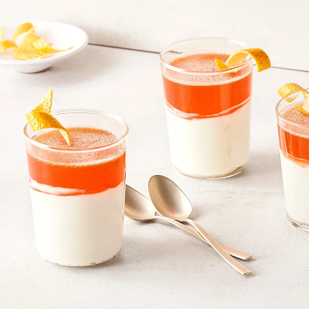 Gläser mit cremigem Dessert und fruchtigem Topping, garniert mit Zitronenzeste, auf einem hellen Untergrund.