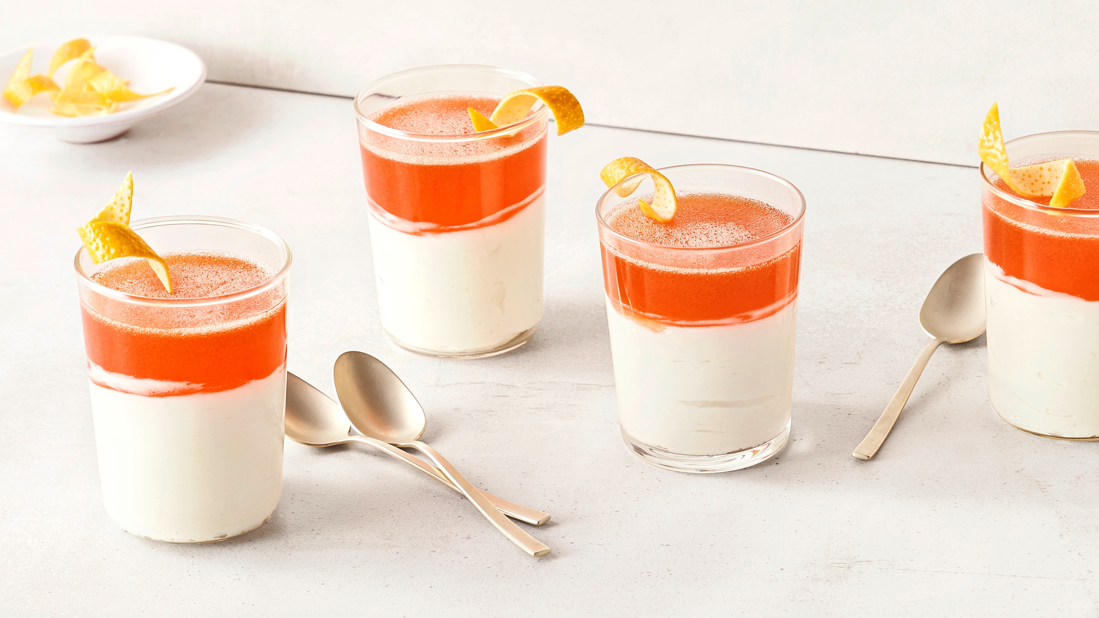 Gläser mit cremigem Dessert und fruchtigem Topping, garniert mit Zitronenzeste, auf einem hellen Untergrund.