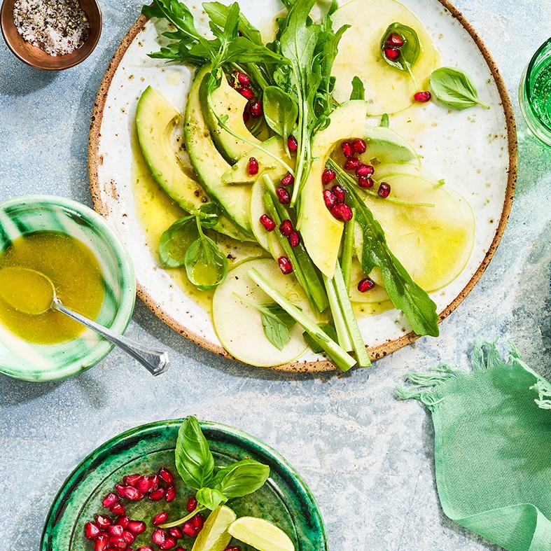 Ein großer Teller mit Apfelscheiben, Avocadoscheiben, Rucolablättern, Granatapfelkernen und Dressing