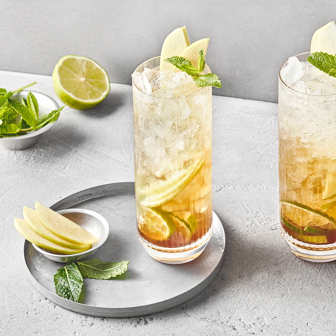 Zwei Cocktailgläser mit Äpfeln, Limetten- und Zitronenscheiben, Eiswürfeln und Minzblättern.