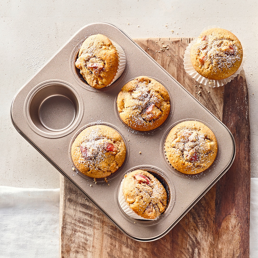 Eine Muffin-Backform mit hellen, fluffigen Muffins mit Apfelstückchen, bestreut mit Puderzucker