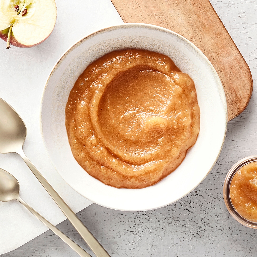 Schale mit Apfelmus. Rechts daneben drei kleinere Glasschalen befüllt mit mehr Apfelmus und etwas Zimt.