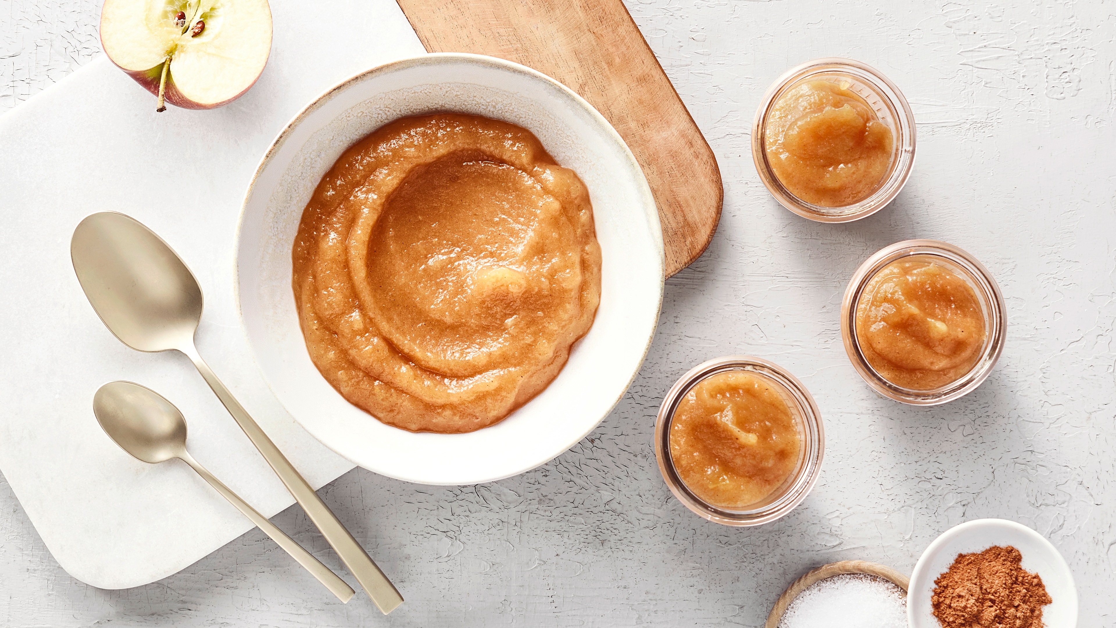 Schale mit Apfelmus. Rechts daneben drei kleinere Glasschalen befüllt mit mehr Apfelmus und etwas Zimt.